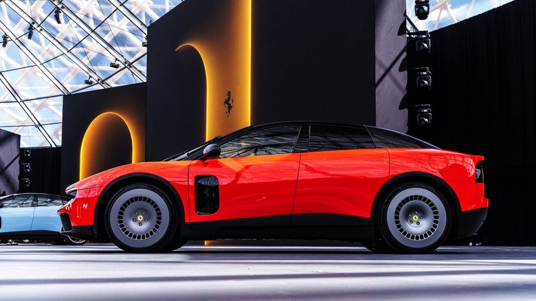 Side profile view of the bright orange Ferrari Luce electric vehicle displayed on a stage with a dramatic black and neon-lit backdrop under a geometric glass dome structure.