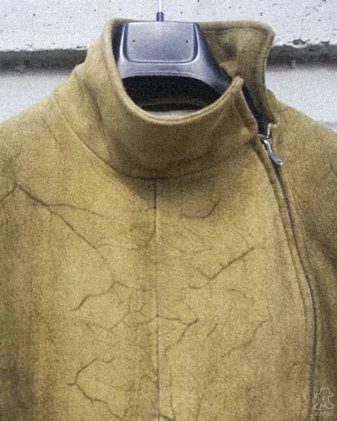 A close up shot of a high neck mustard yellow jacket by Carol Christian Poell featuring visible dark vein like lines from the injected dyeing process.