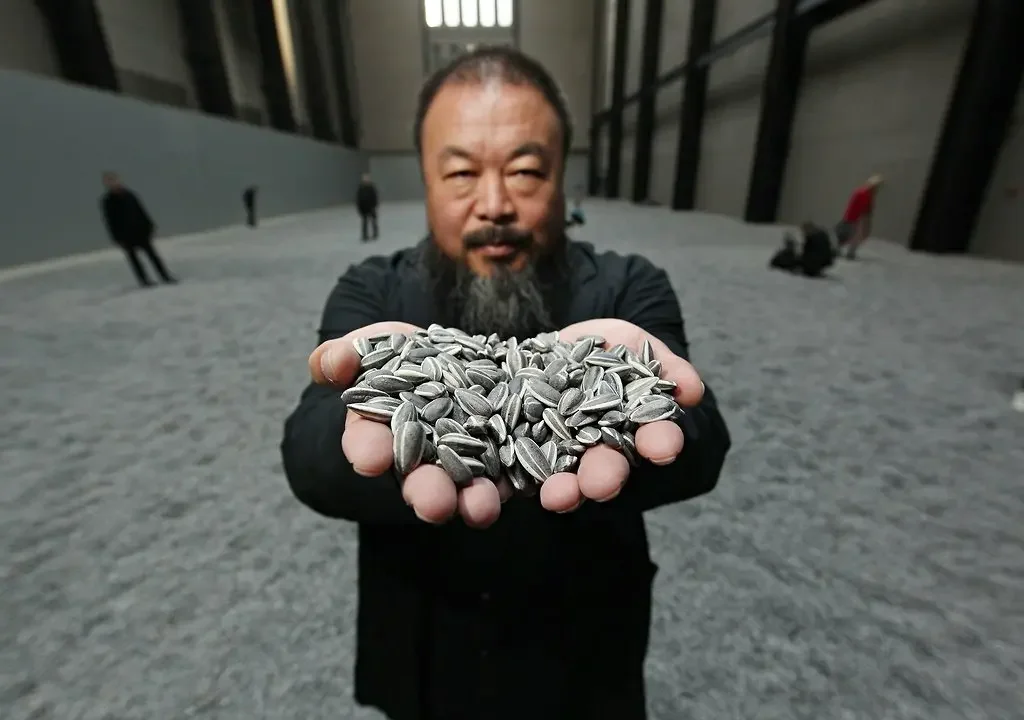 Artist Ai Weiwei holding a handful of his porcelain sunflower seeds from the 'Sunflower Seeds' installation at the Tate Modern, representing activist art.