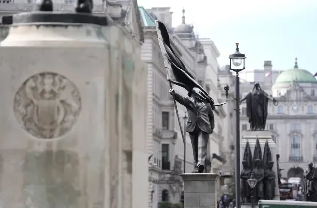 A wide shot of the Banksy statue The Suited Void in Waterloo Place London with the Guards Crimean War Memorial and historic architecture visible in the background.