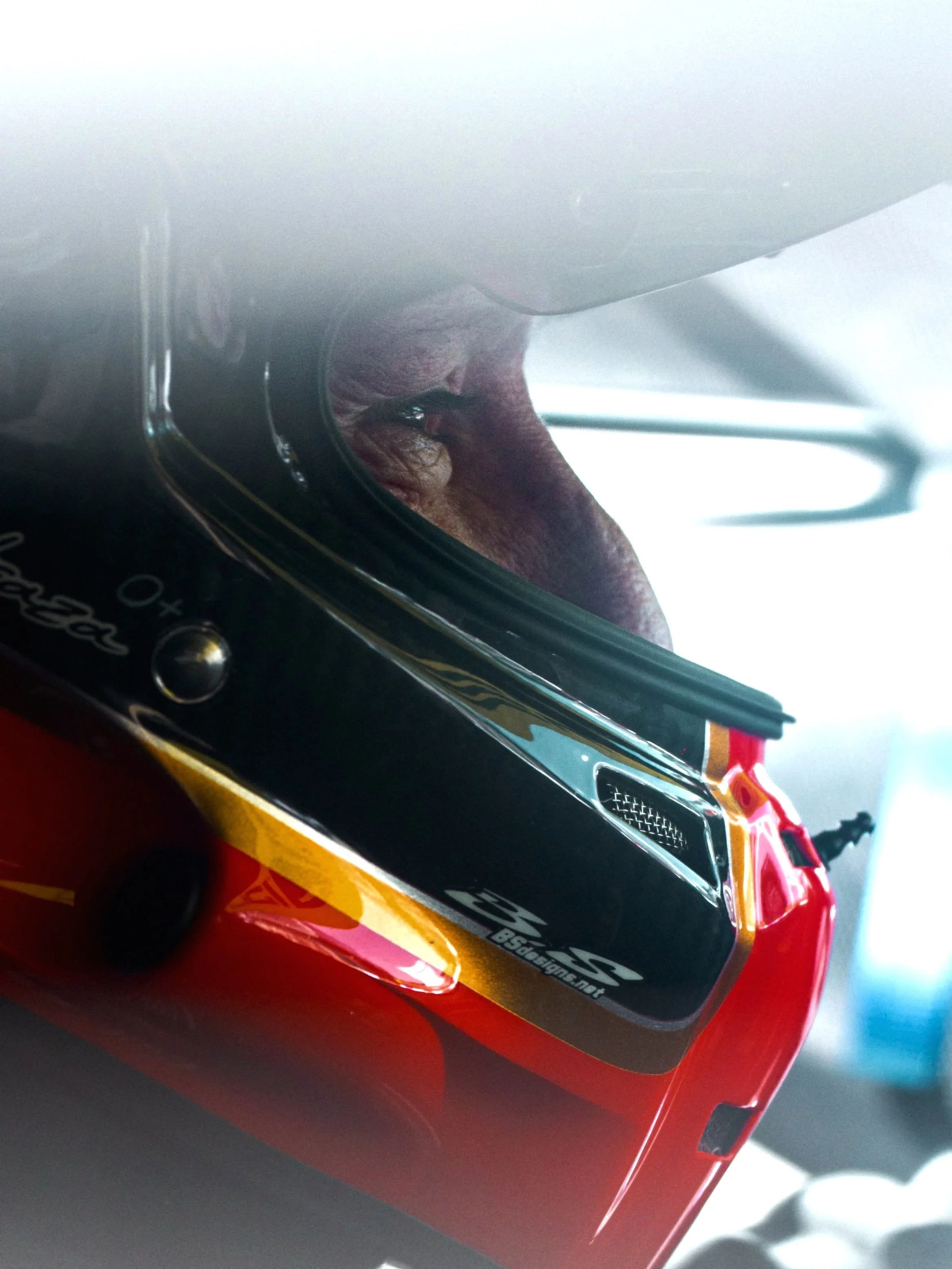 Close-up of a race car driver wearing a red racing helmet and visor, looking out from inside the helmet.