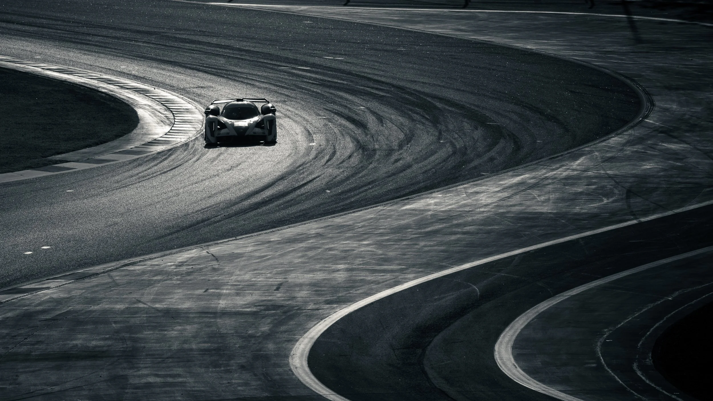 A black and white sports car on a curving race track with tire marks visible on the asphalt.