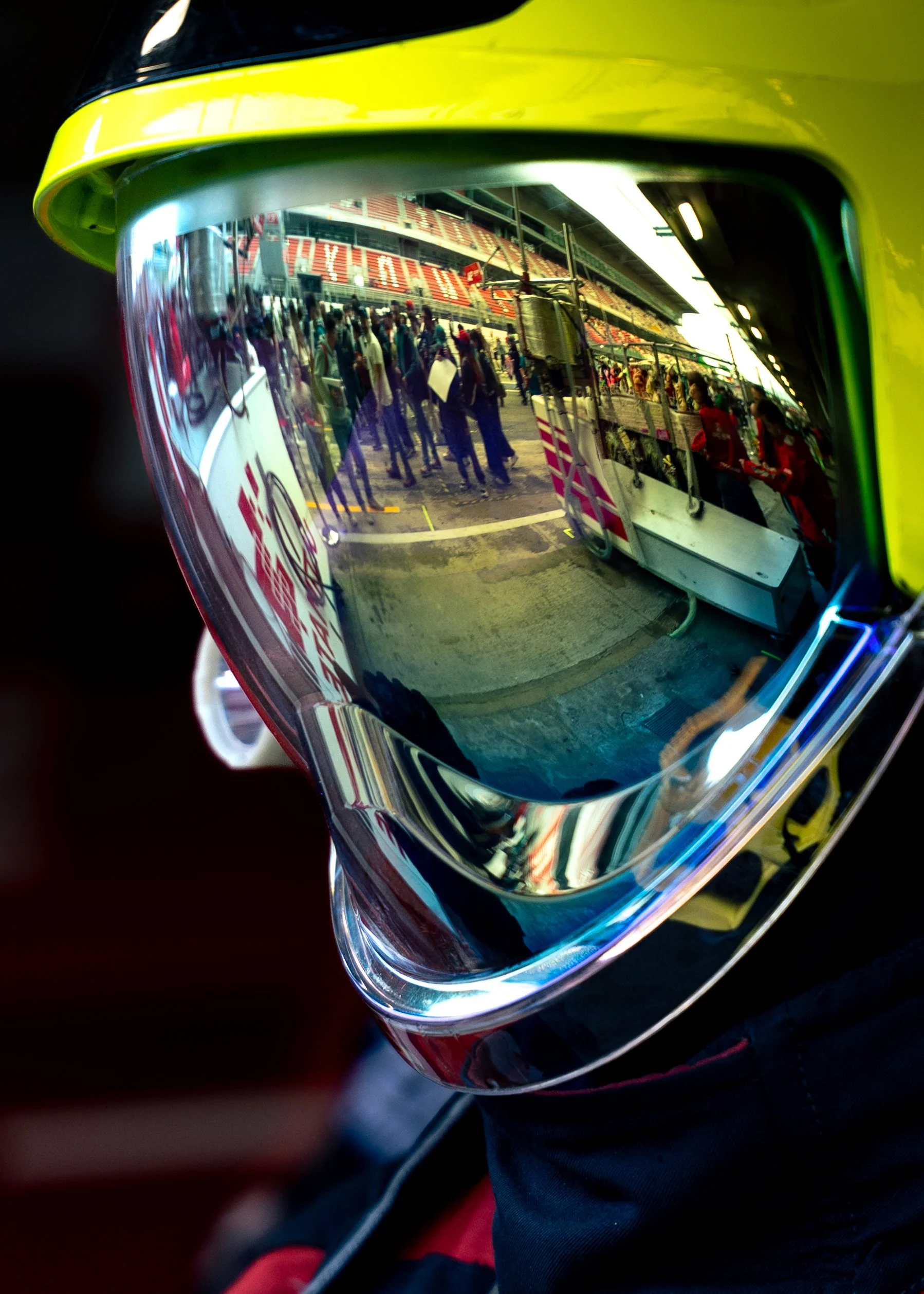 Reflection of a busy outdoor scene with people, stands, and seating area, seen through the mirrored visor of a yellow helmet.