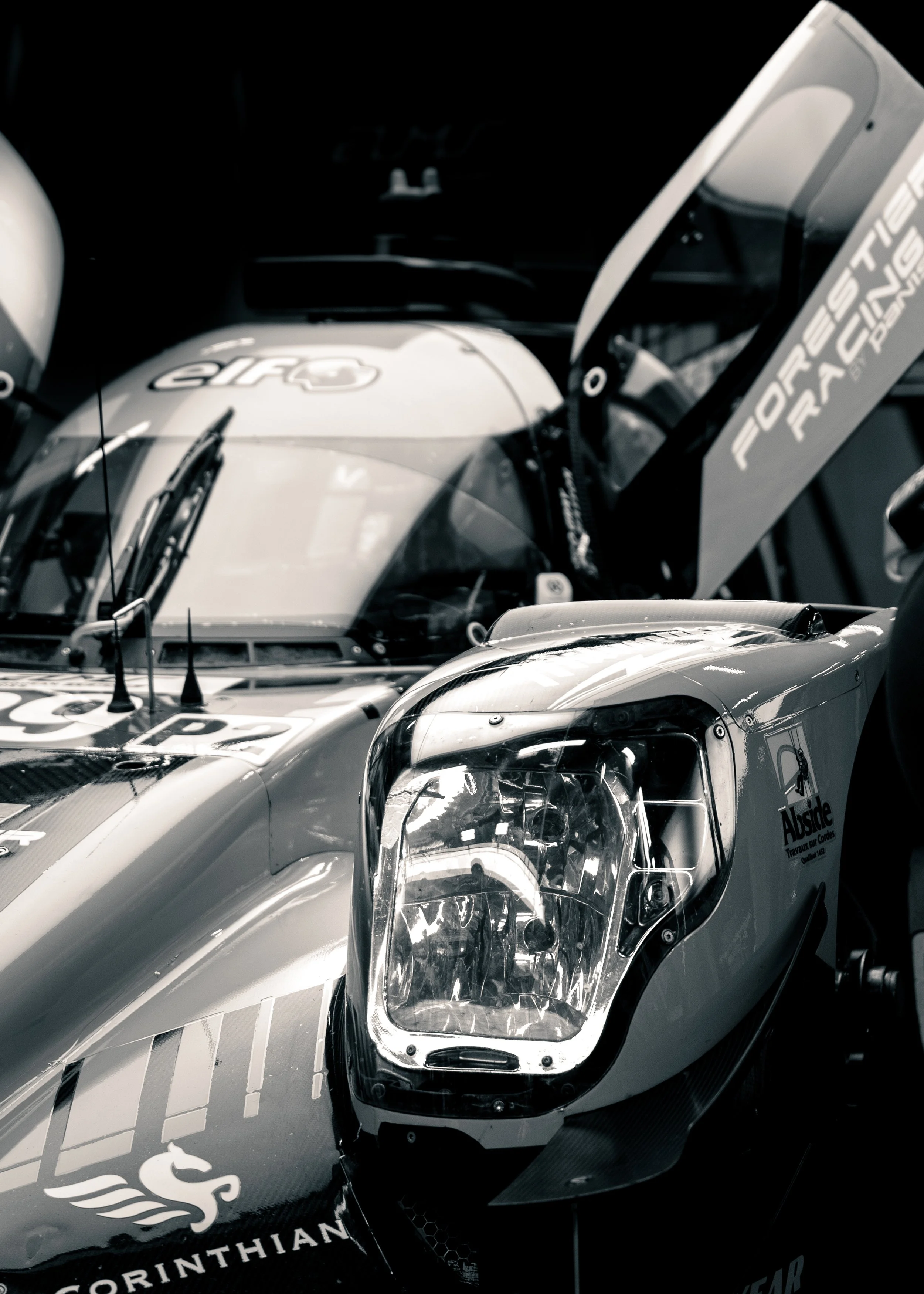Close-up of a racing car with a visible headlight and partially covered with a black and white striped livery, featuring sponsor logos.