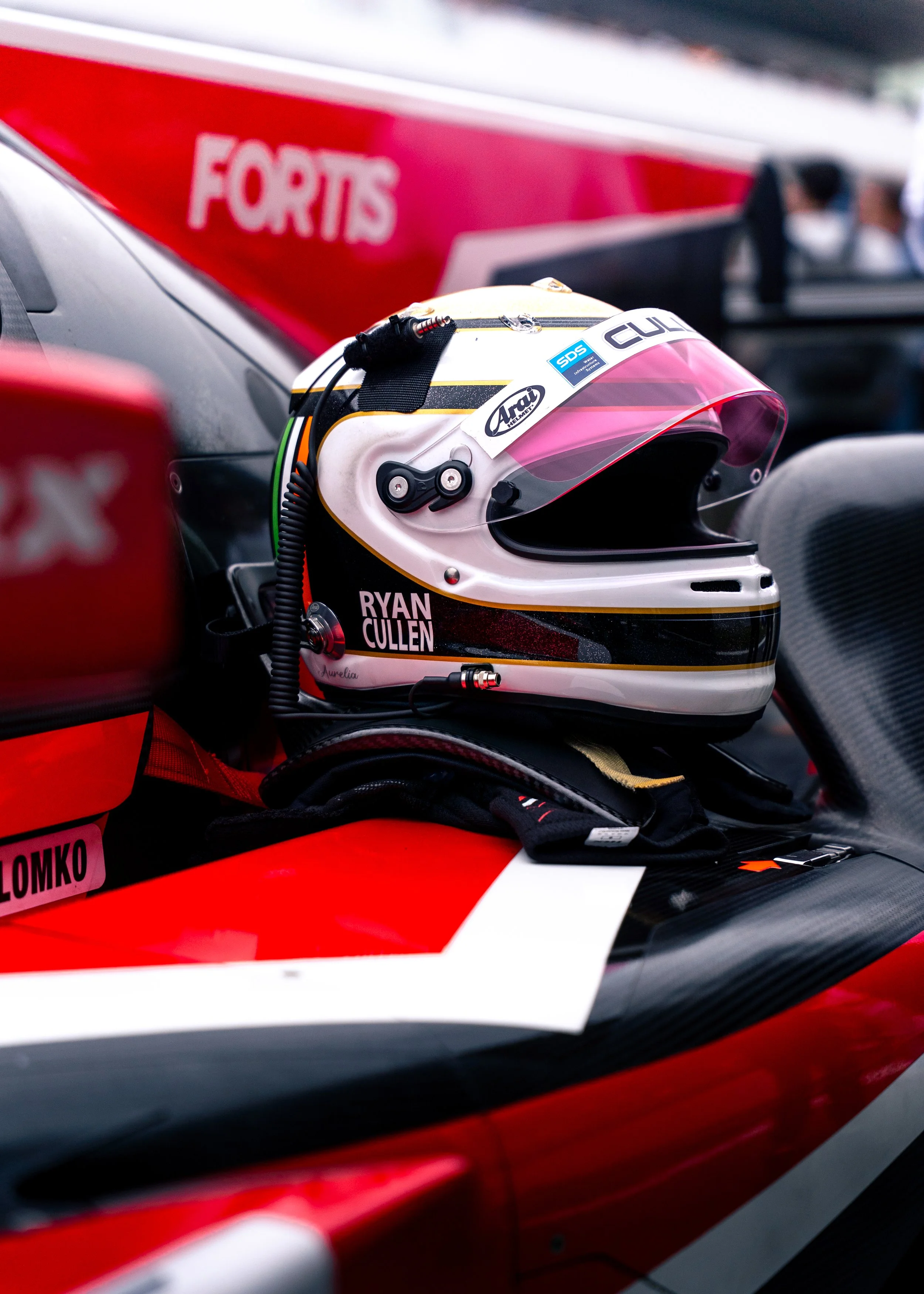 Close-up of a racing helmet placed on the car's cockpit, with a red and black race car visible in the background.