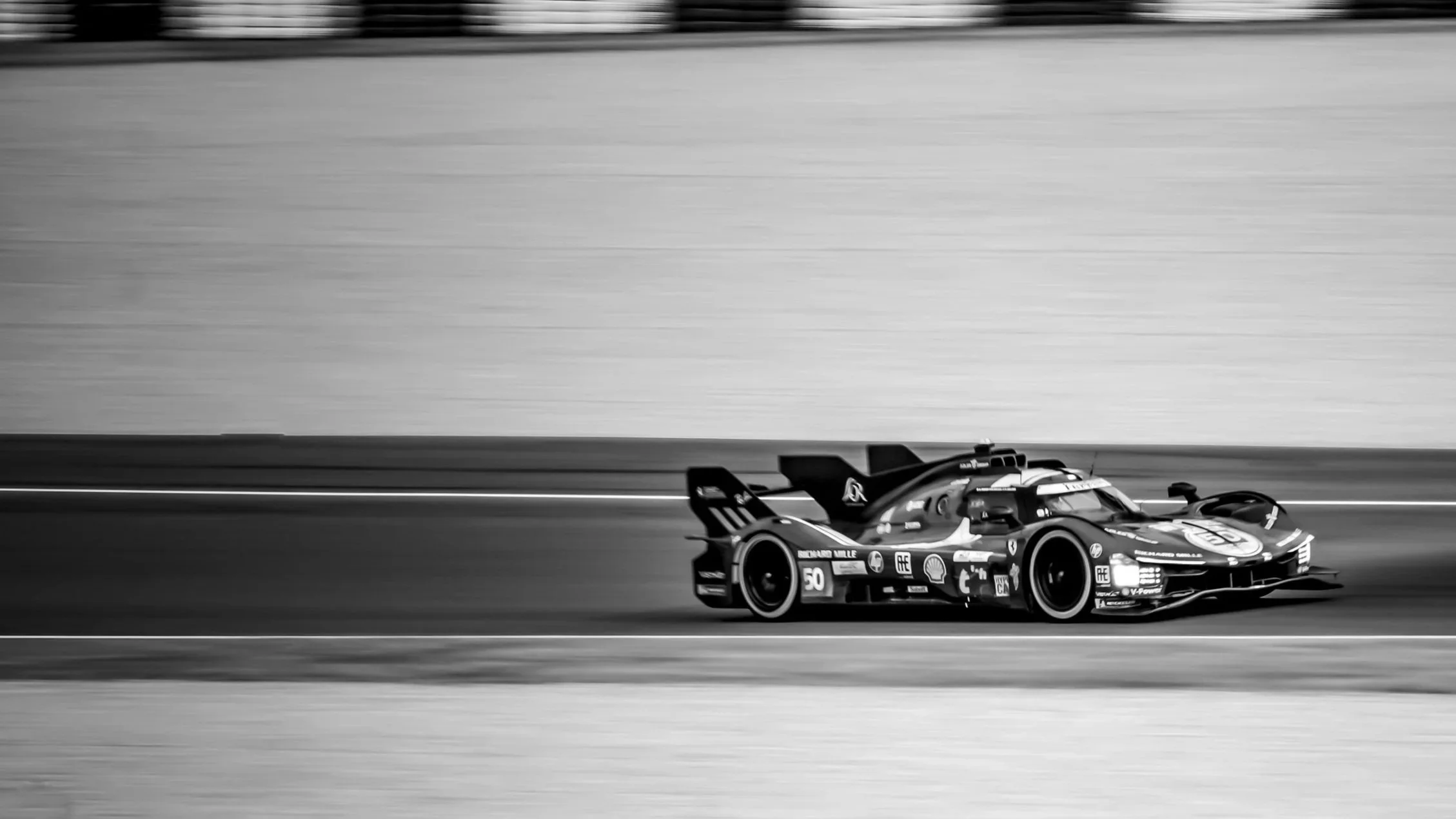 Black and white photo of a race car driving on a track with a plain background.