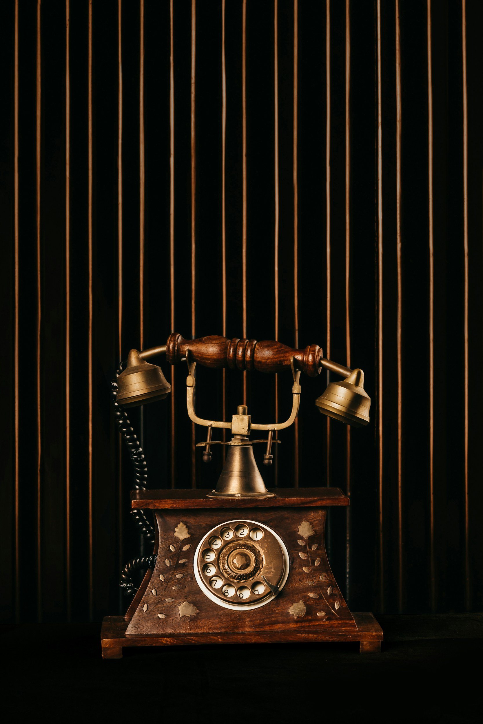 Antikes Telefon mit Wählscheibe vor dunklem Hintergrund mit vertikalen goldfarbenen Linien.
