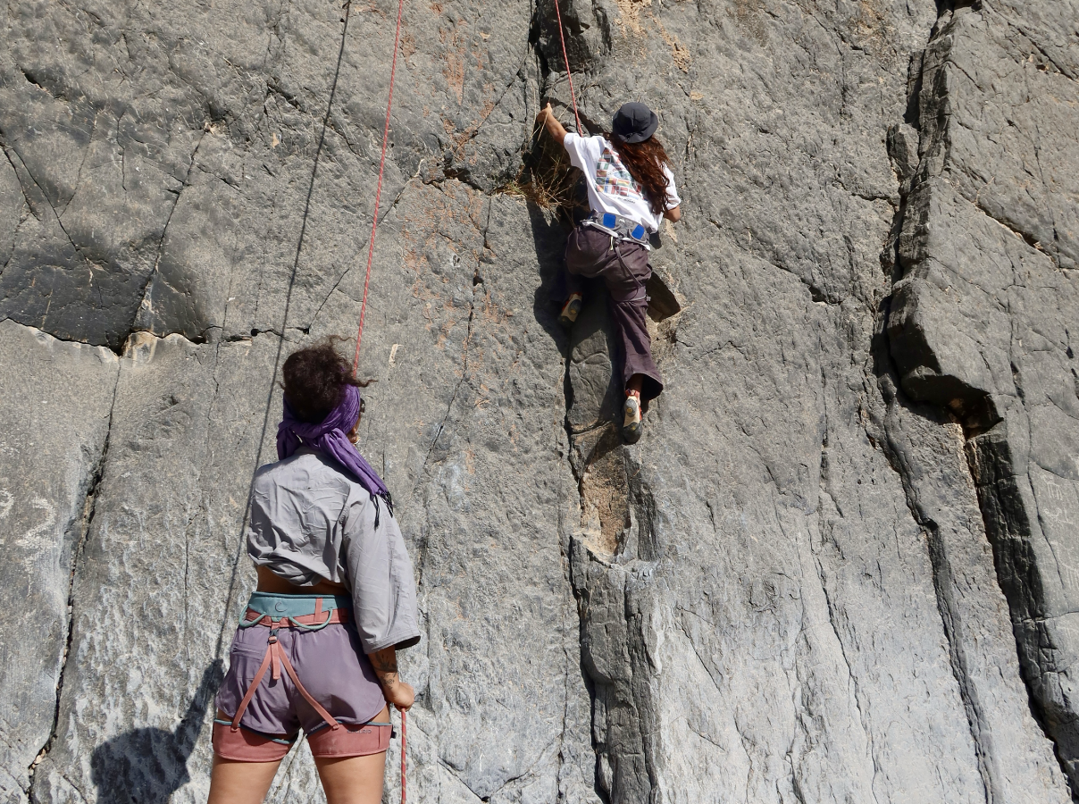 A woman climbing a rock face while another woman belays her on the ground.
