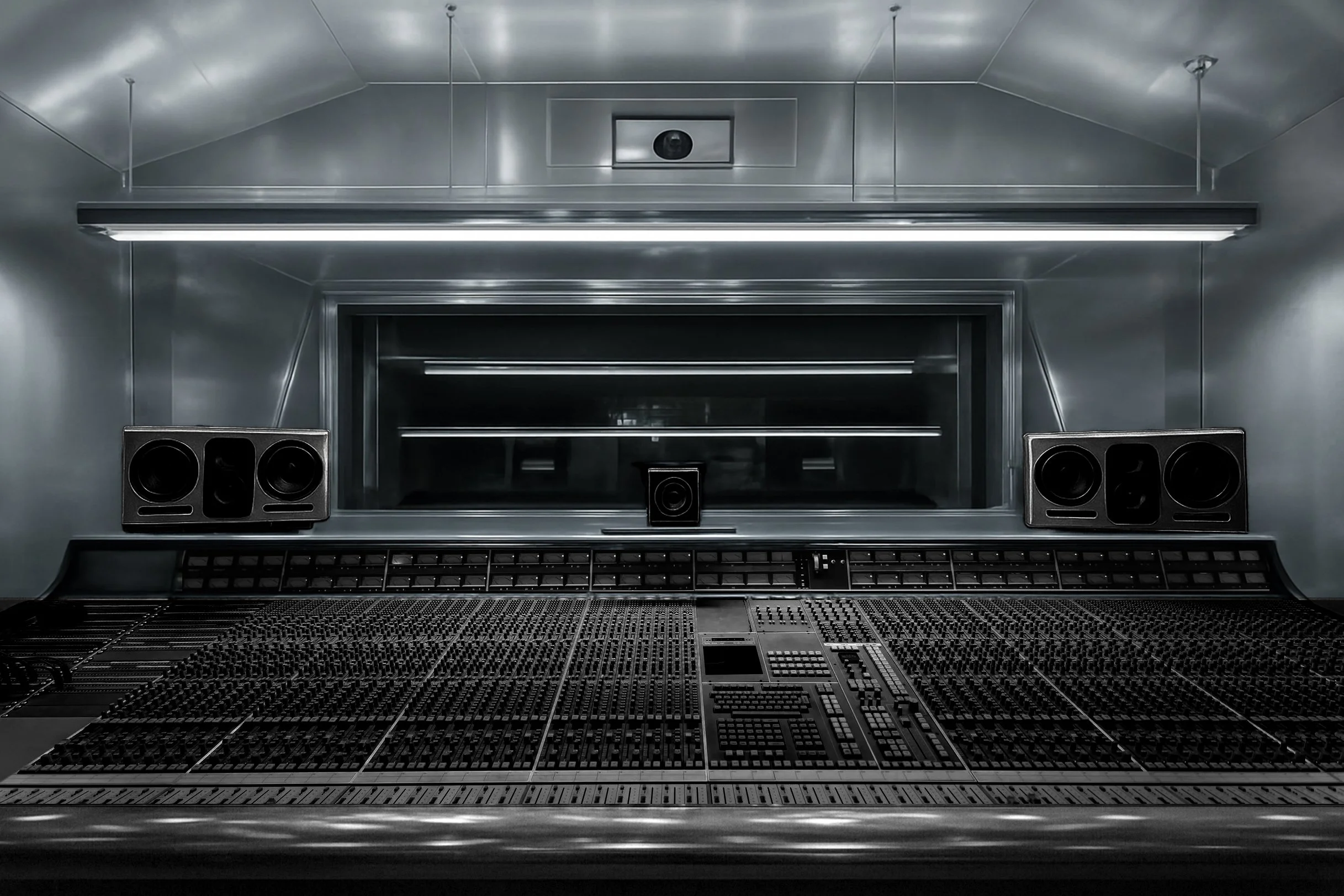 Sound mixing studio with a large audio mixing console, speakers, and a window into a control room.