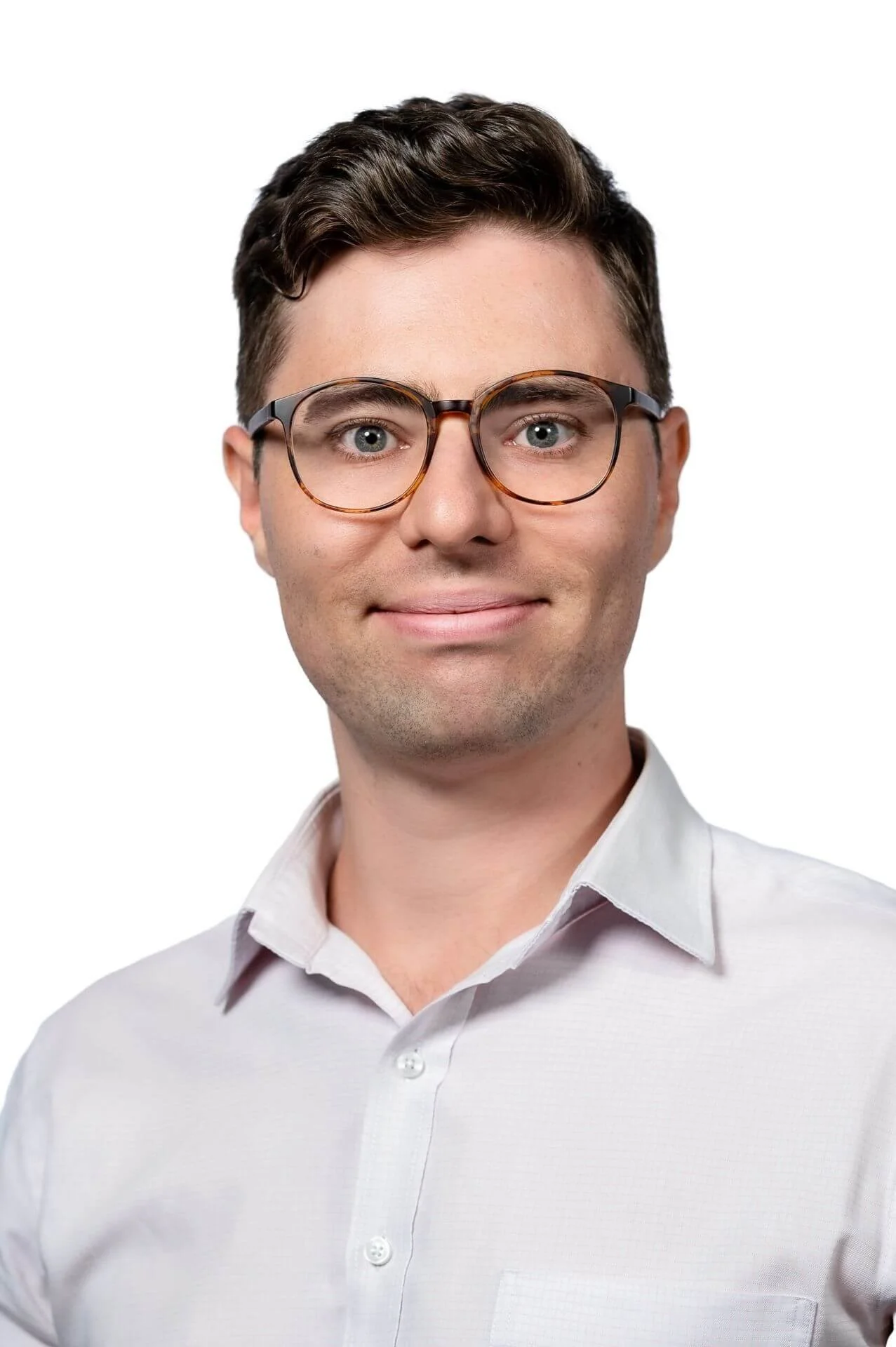 A young man with dark hair wearing glasses and a white button-up shirt, smiling against a plain white background.