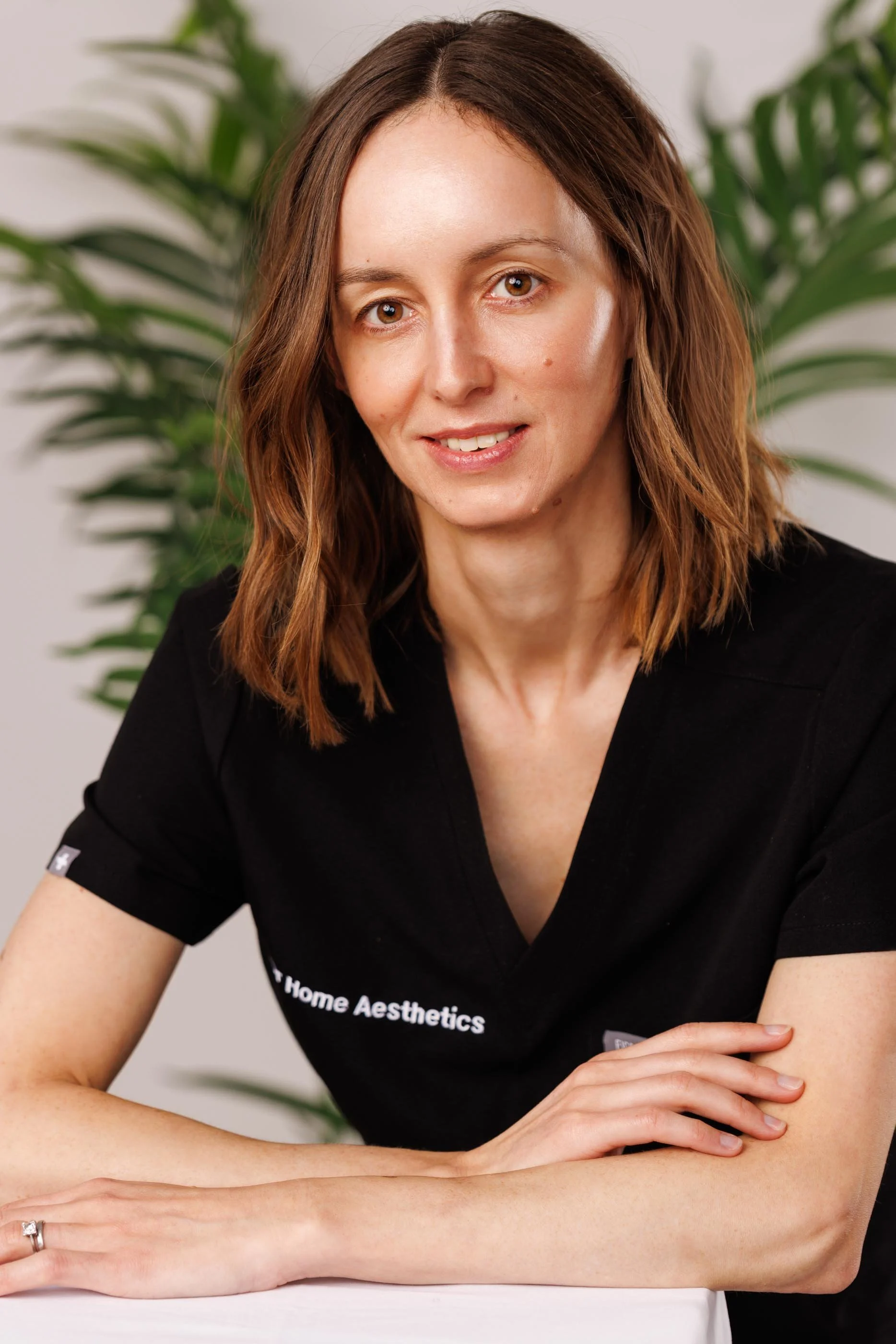 A clean, natural light portrait of a healthcare professional in a branded black uniform, arms resting forward, relaxed and approachable expression. Bright background with foliage, no studio artifice. This image solves a specific and common problem — 