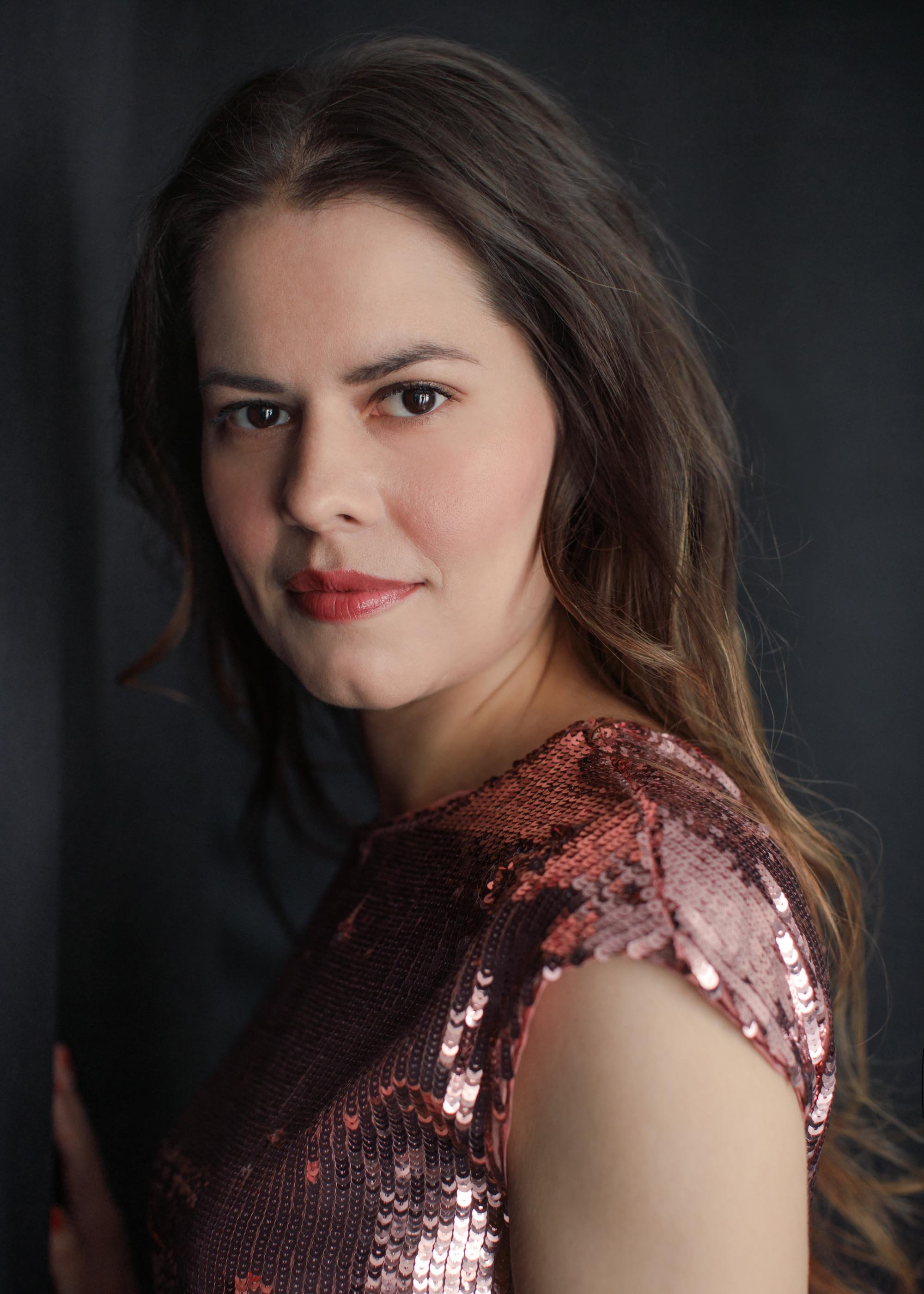 elegant woman wearing sequined dusty rose dress photographed against black backdrop and looking into camera