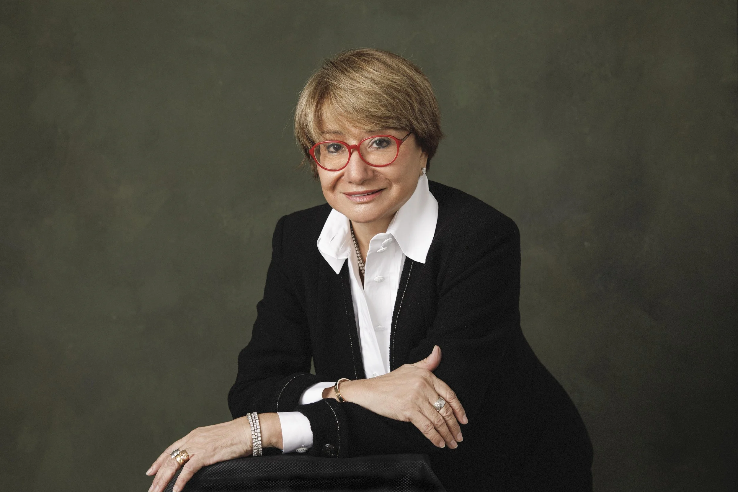 Elegant woman with red frame eye glasses in a black suit and white shirt against canvas backdrop photographed in private photo studio in East Lothian by Angelique Portrait Photography