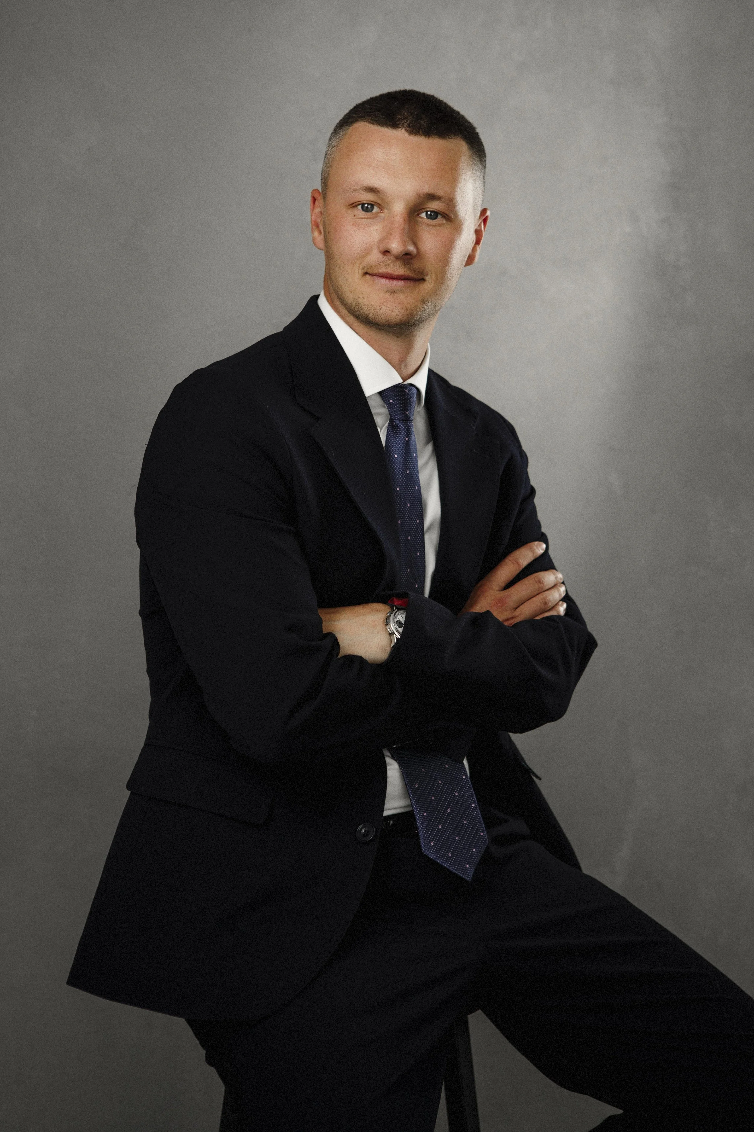 Young Scottish man in a tailored navy business suit, fine art portrait against hand-painted studio backdrop, East Lothian