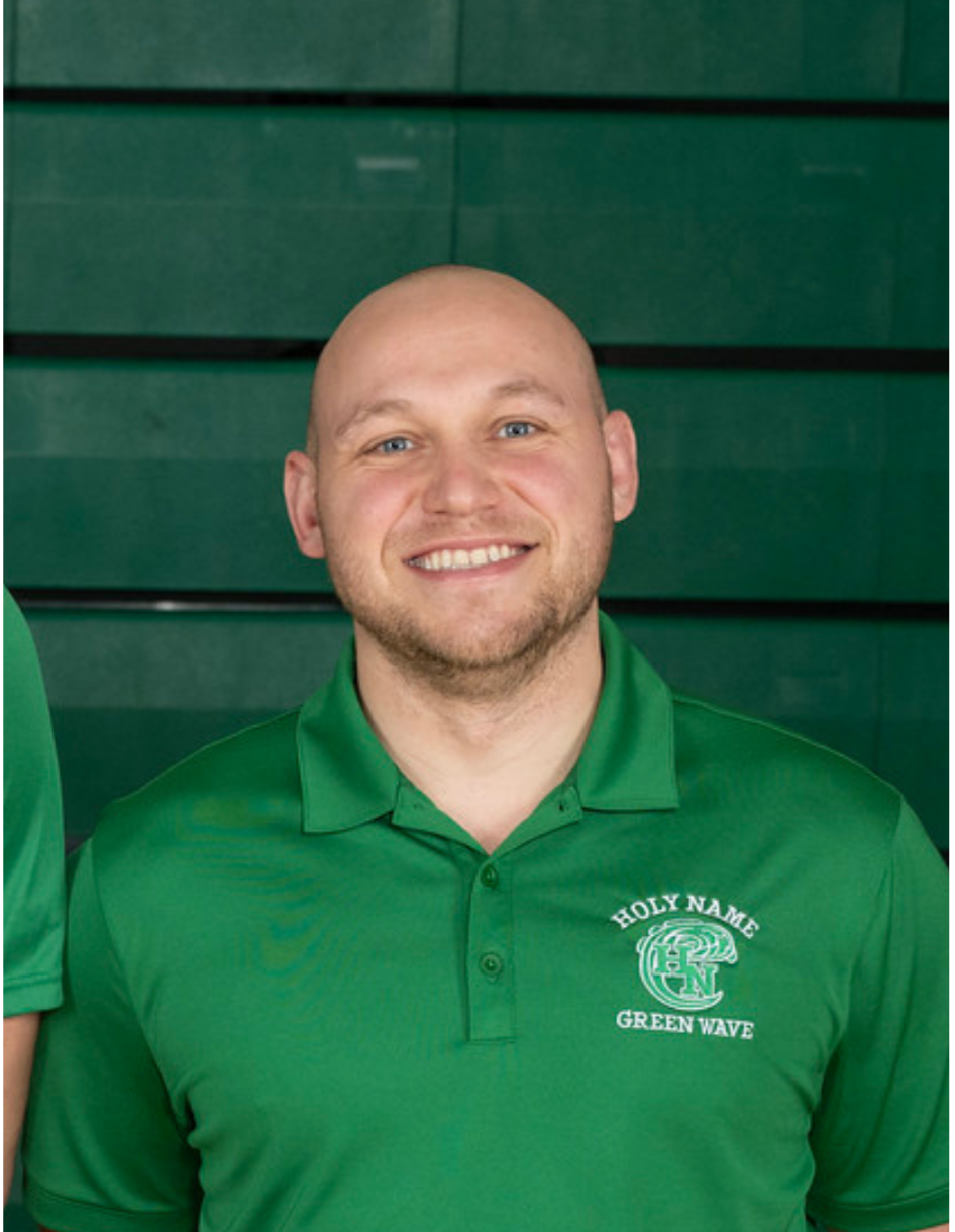A smiling man with a shaved head and beard wearing a green polo shirt with 'Holy Name Green Wave' logo, standing in front of a green background.