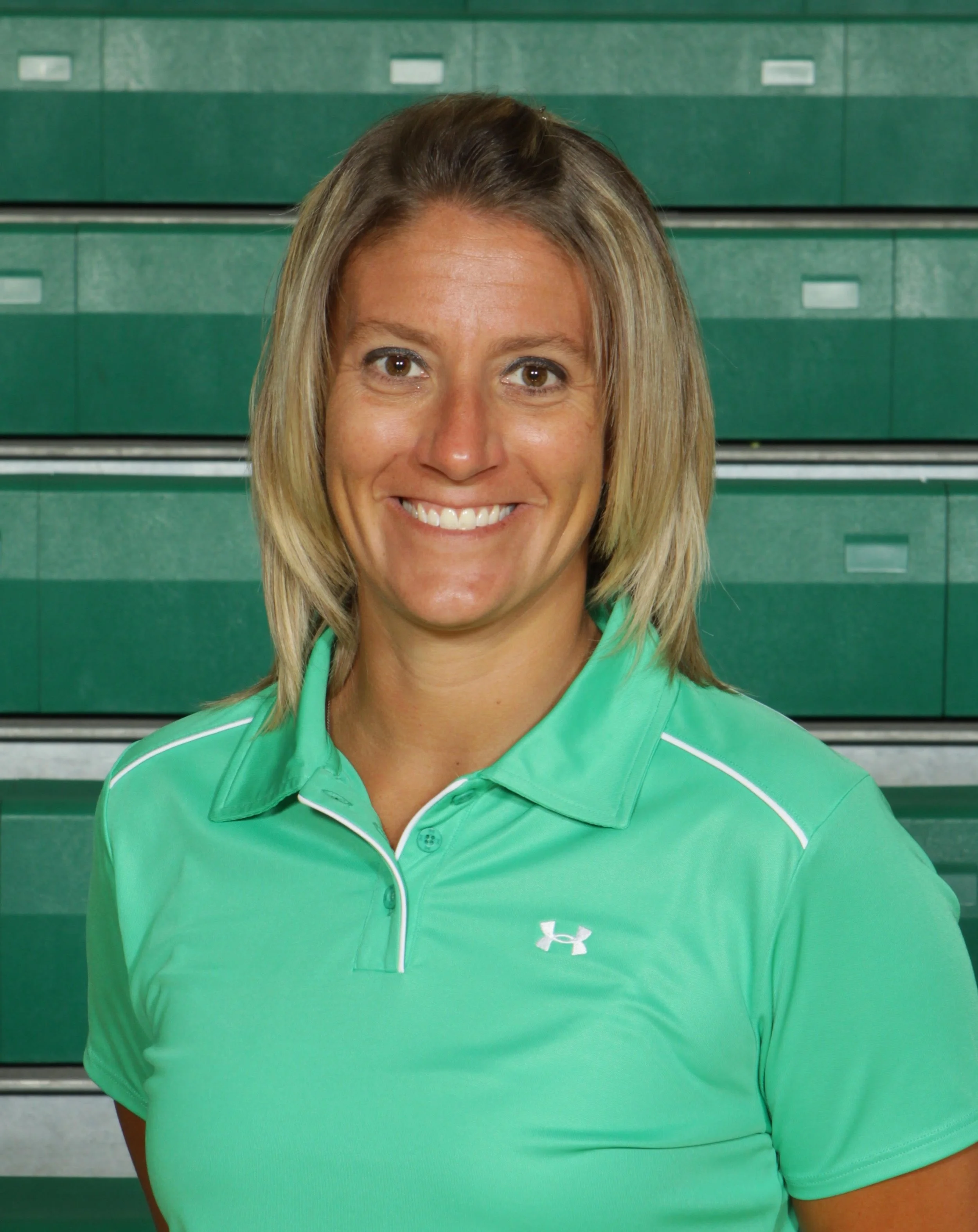 Portrait of a woman wearing a green Under Armour sports shirt, smiling in front of green stadium seats.