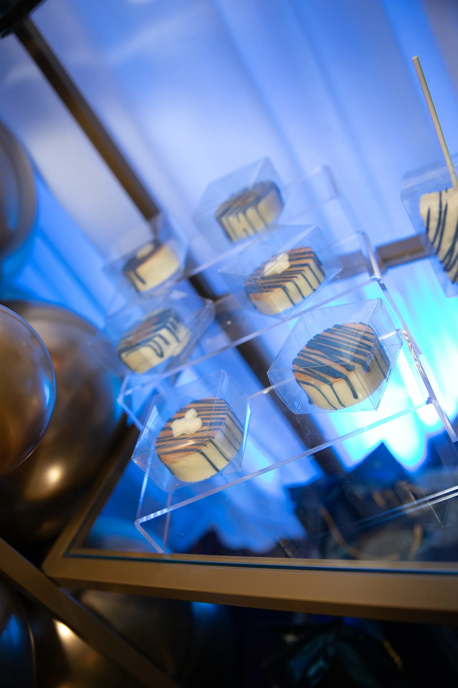 Assorted decorated cookies displayed in a clear acrylic case under blue lighting.