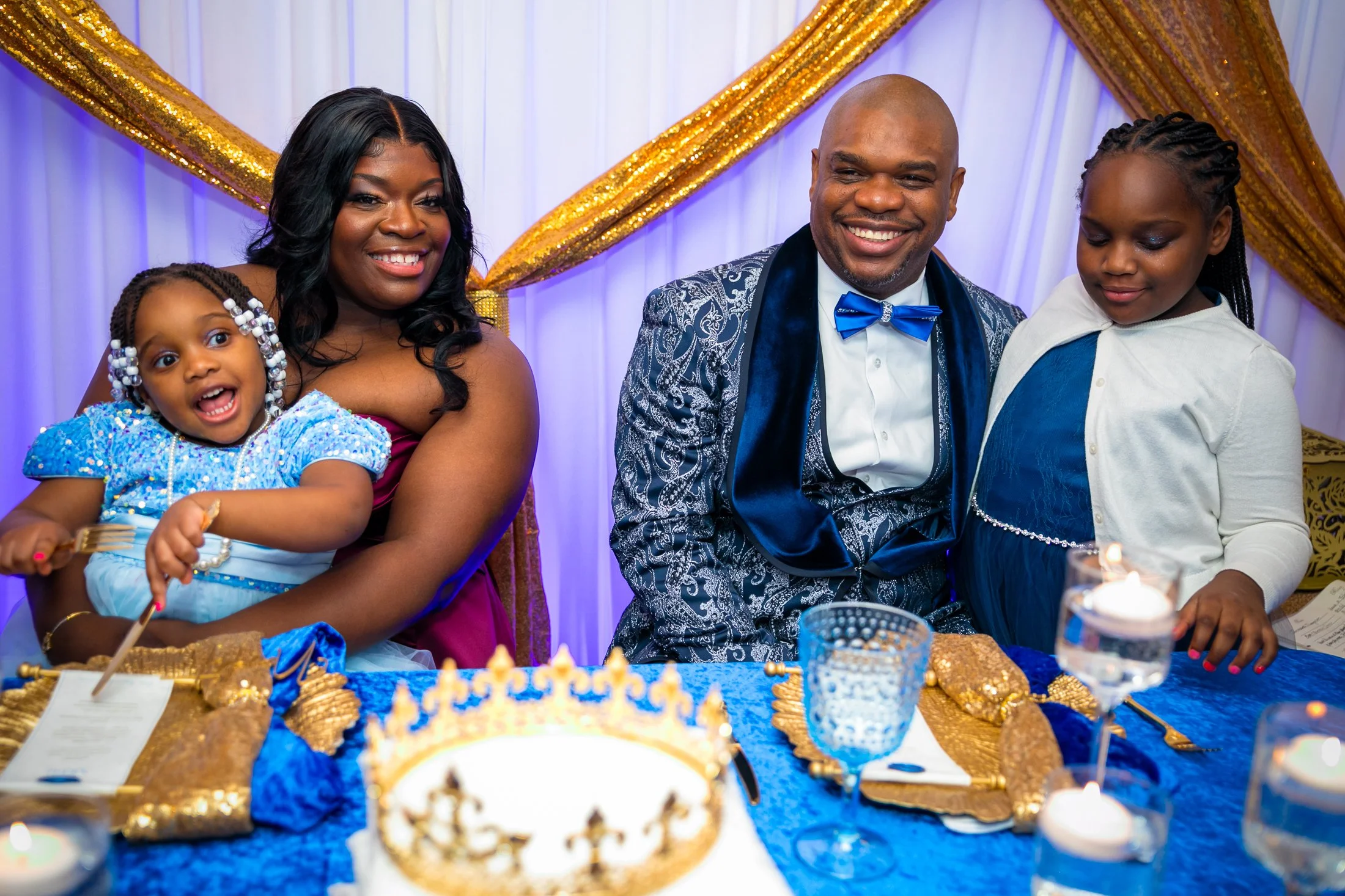 A family celebrating a birthday or special occasion at a decorated table with a cake and candles, smiling and posing for the photo.