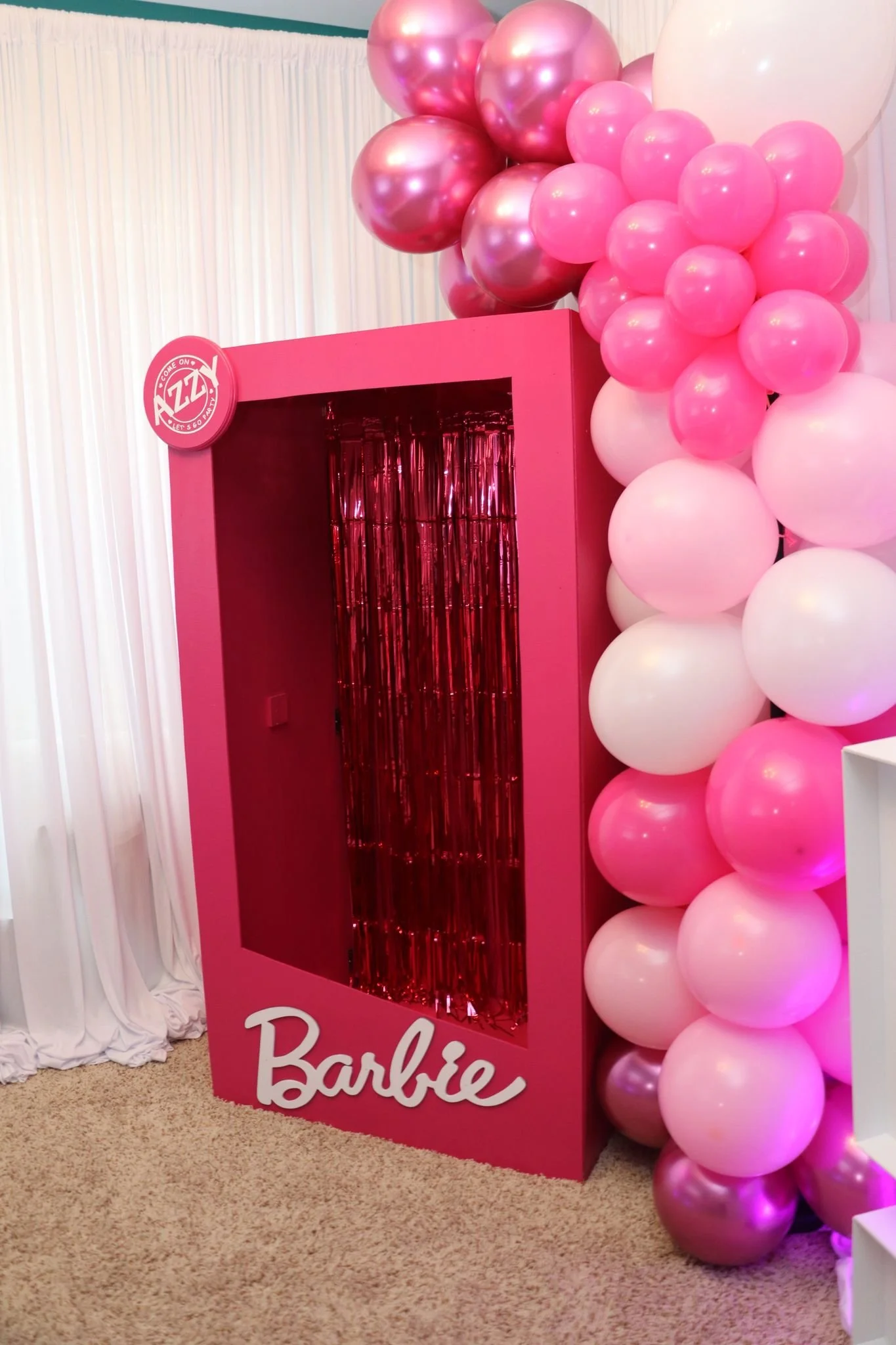Pink Barbie-themed photo booth with balloon arch in pink and white, and a pink frame with red tinsel inside, labeled 'Barbie' at the bottom.