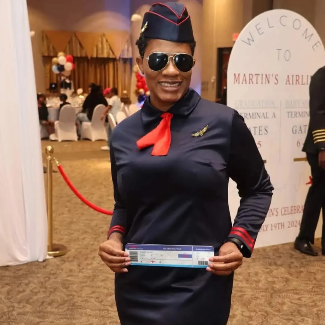 A woman dressed as a pilot, wearing sunglasses, a pilot hat, and a uniform with a red scarf, holding a boarding pass at Martin's Airport celebration event.