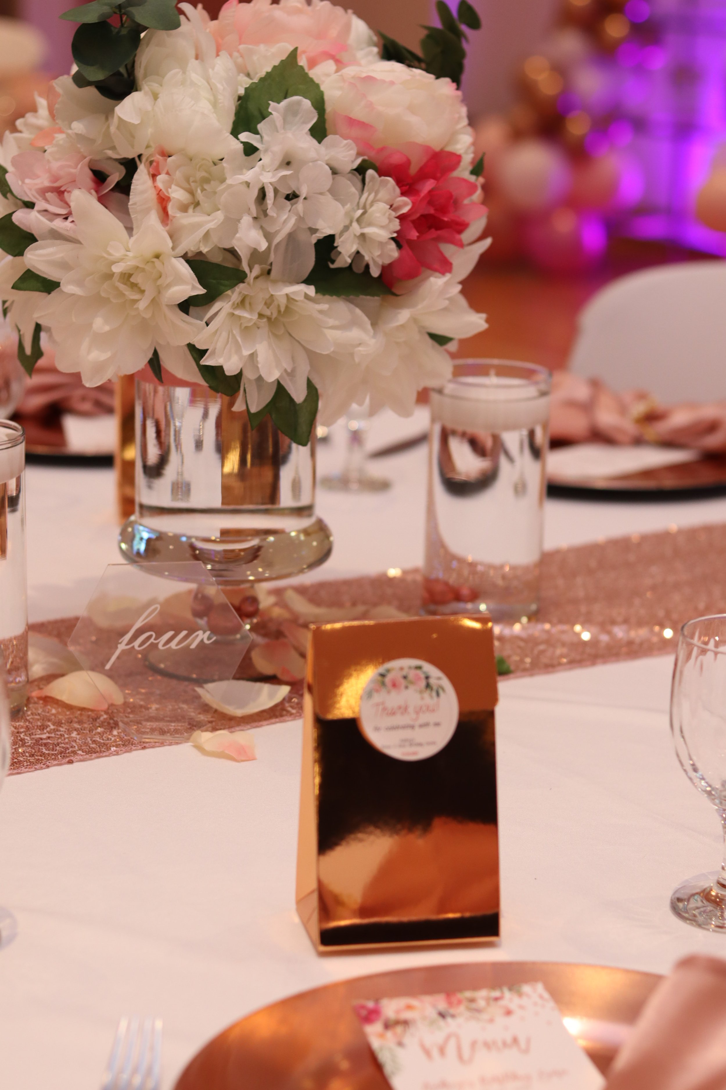 A centerpiece with pink and white flowers in a metallic vase on a decorated table during a celebration.