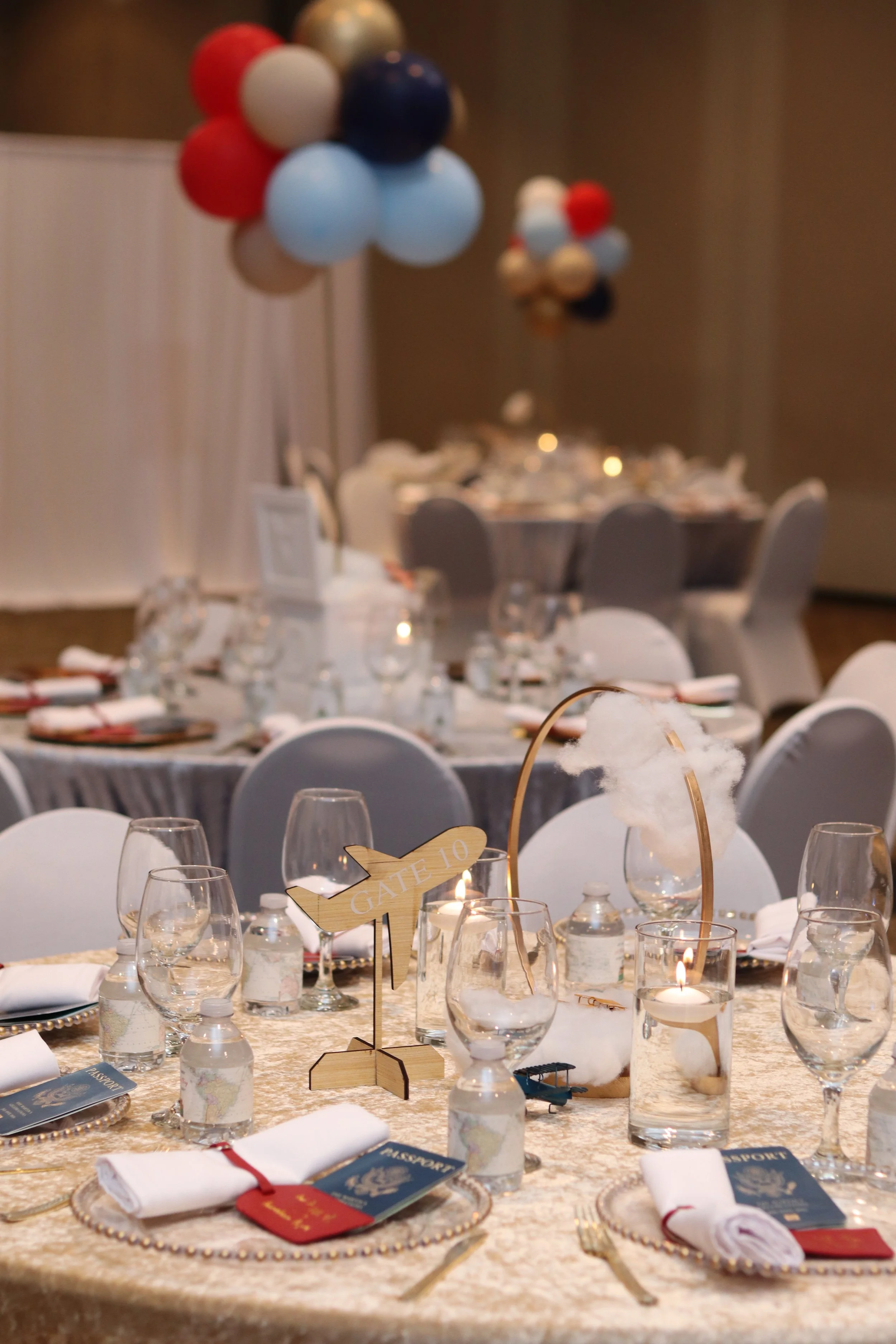 Decorated banquet table with place settings, water bottles, candles, a cotton candy centerpiece, and balloon displays in the background at an event venue.