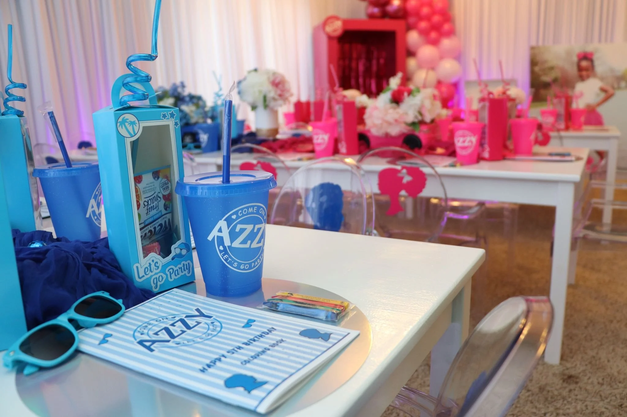 Decorated party table with pink and blue themed items, including drinks, balloons, flowers, and photo props.