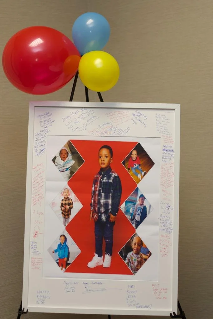 A birthday poster of a young boy surrounded by handwritten messages and signatures, decorated with red, yellow, blue, and orange balloons.