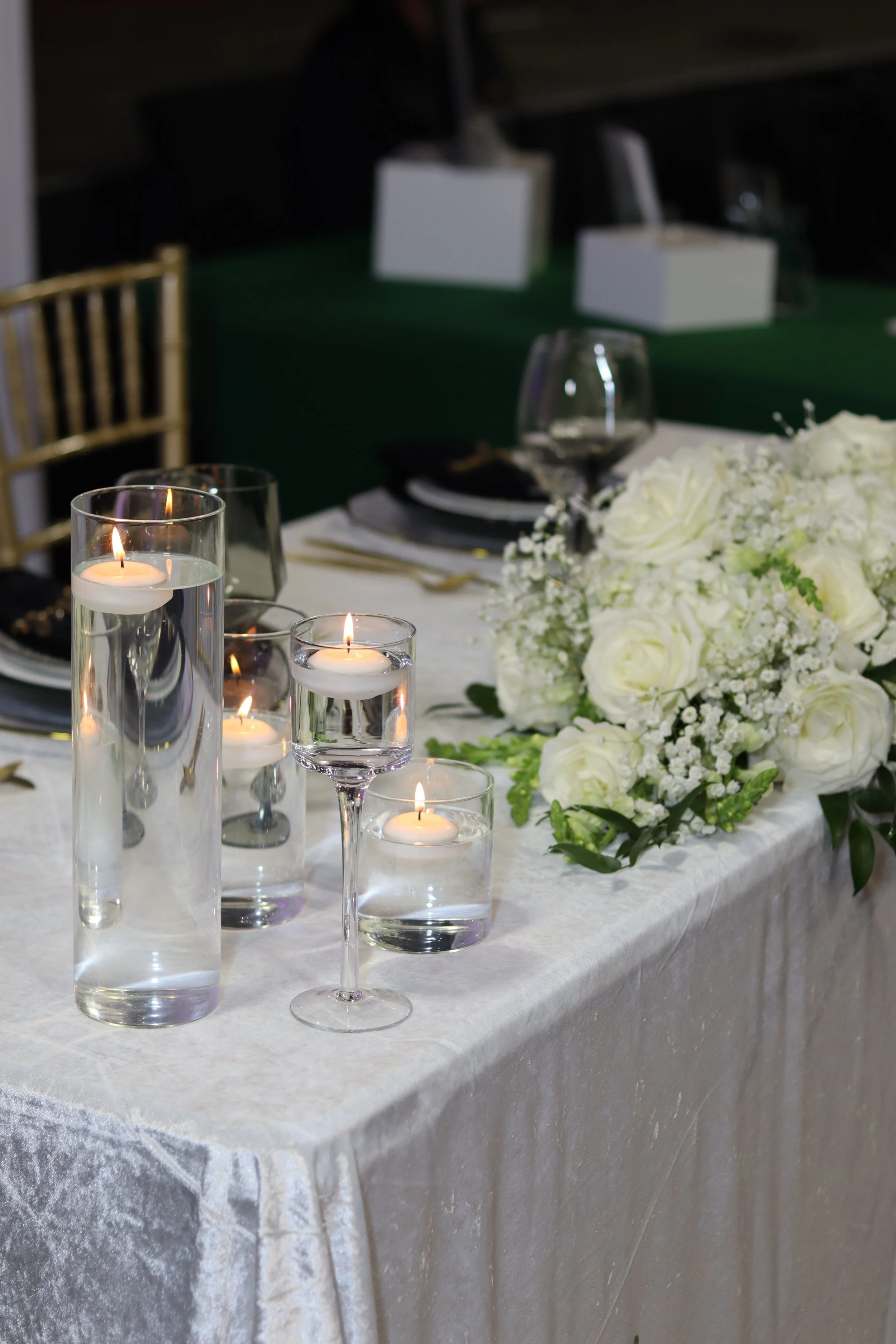 A table decorated for a special occasion with white flowers, candles in glass holders, and empty wine glasses.