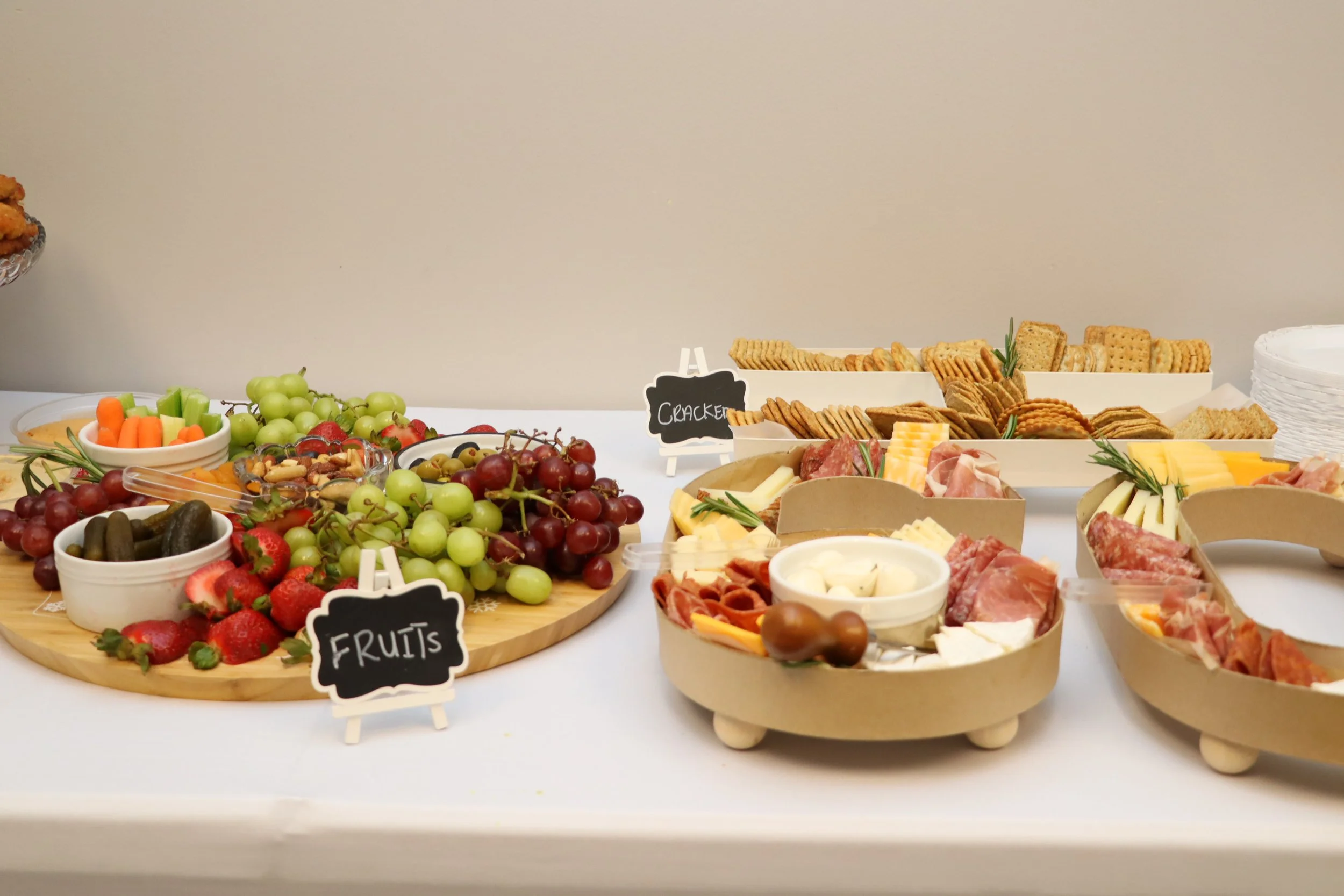 Fruits and cheese platter with grapes, strawberries, pickles, and crackers, on a table.