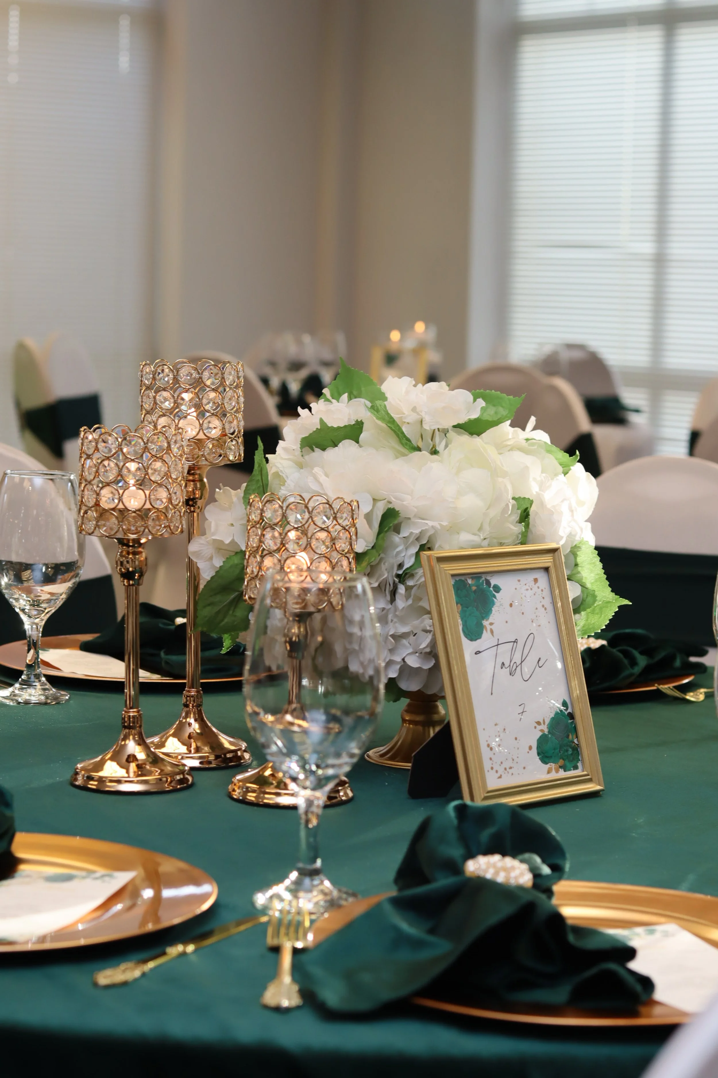 Decorated banquet table with white floral centerpiece, gold tableware, green napkins, wine glasses, and candle holders, set for a formal event.