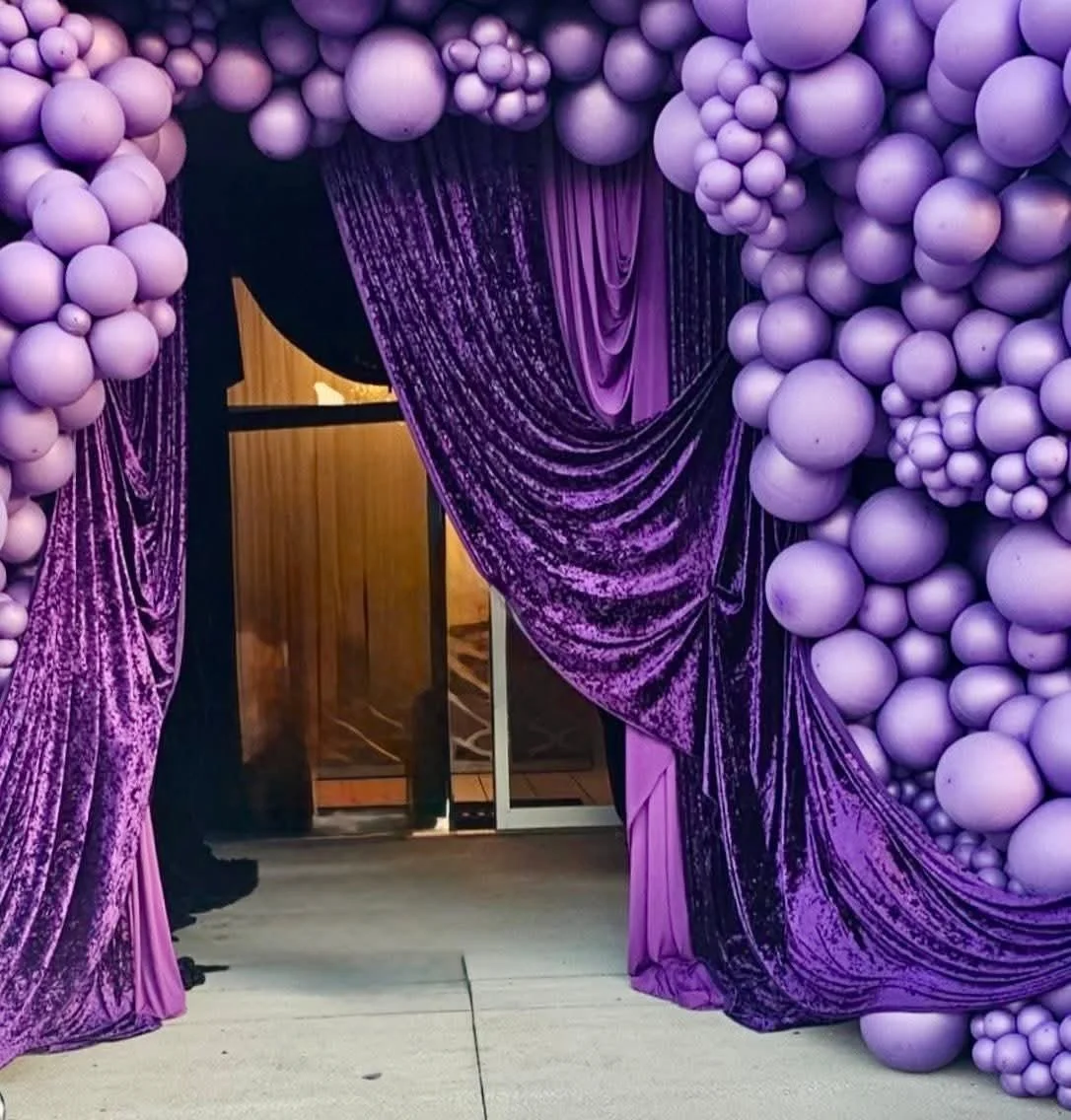 Purple balloon arch with velvet curtains leading into a decorated space