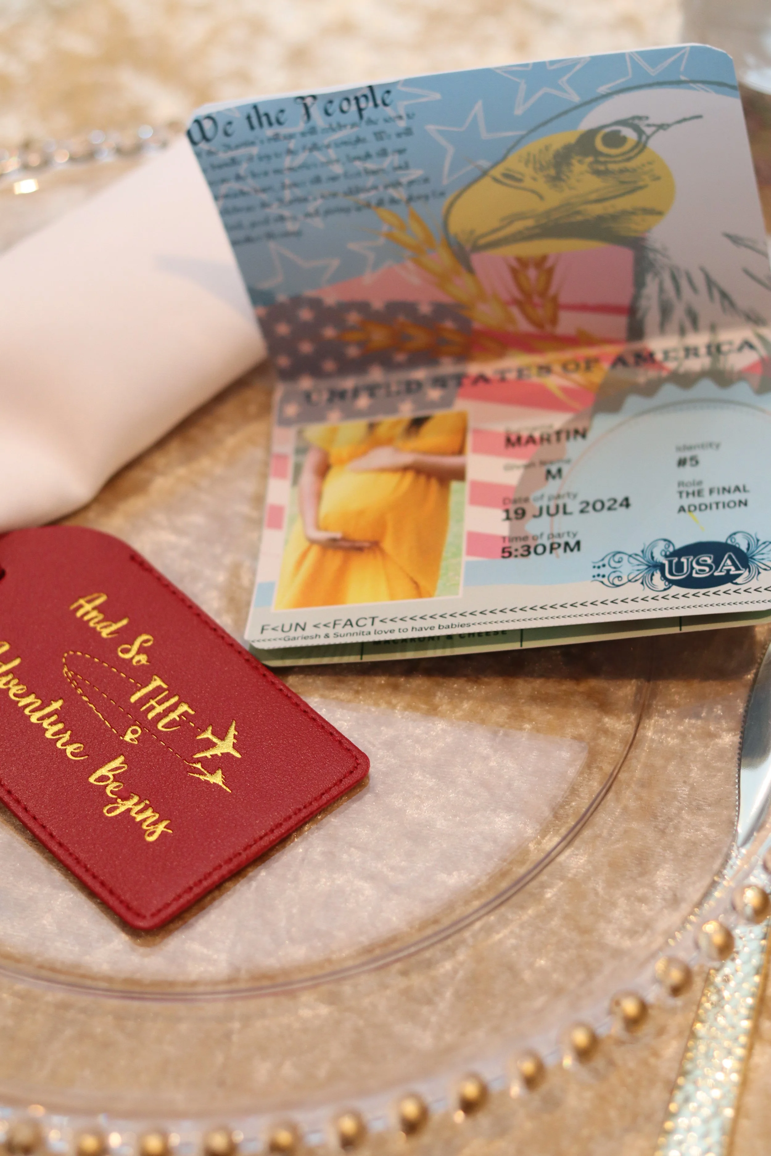 A portion of a passport, a red travel patch with gold embroidery, and a US passport page with a photo of a pregnant woman in a yellow dress, displayed on a decorative tray.