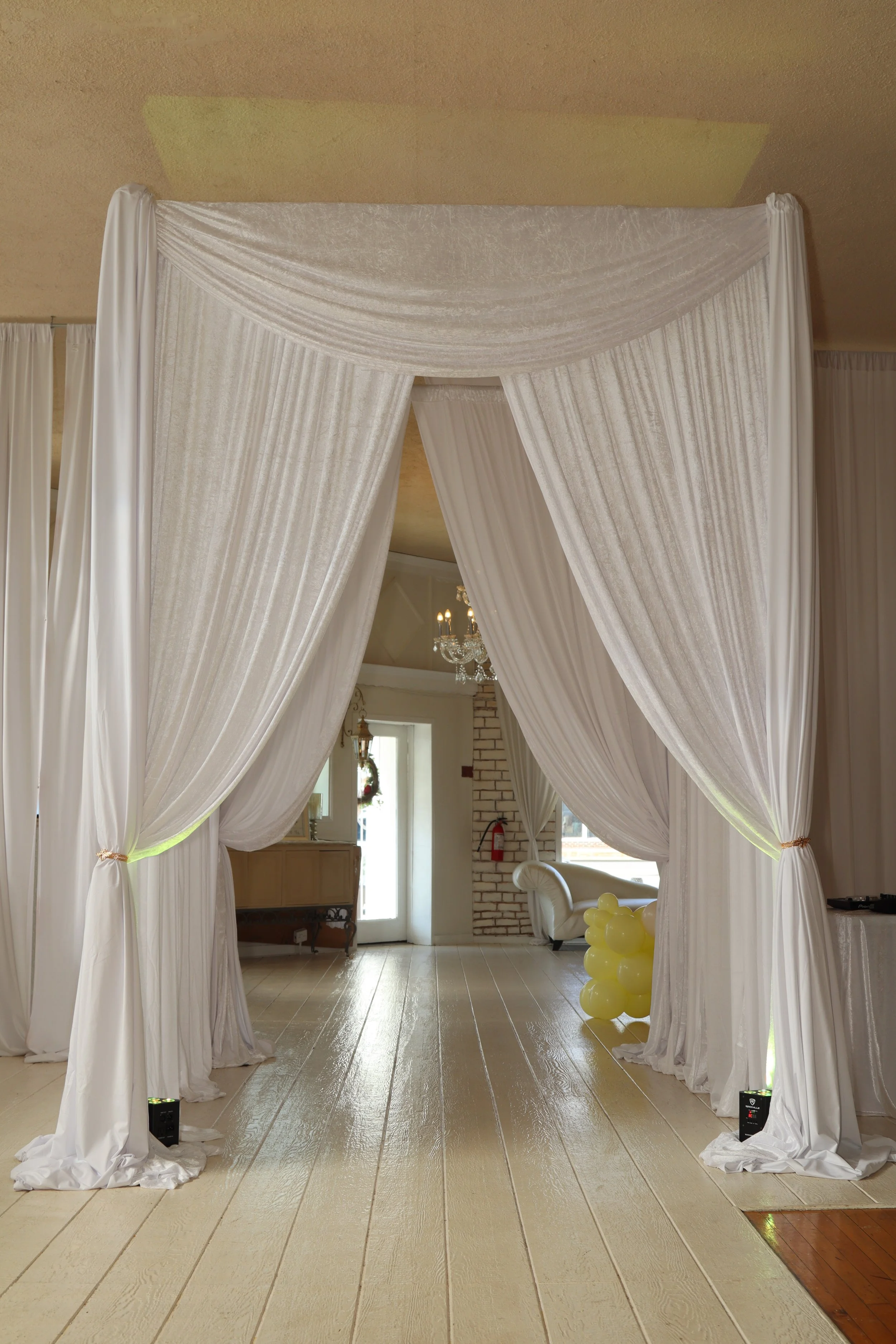 Elegant white draped curtains forming a doorway or partition in a decorated room with balloons and chandelier.