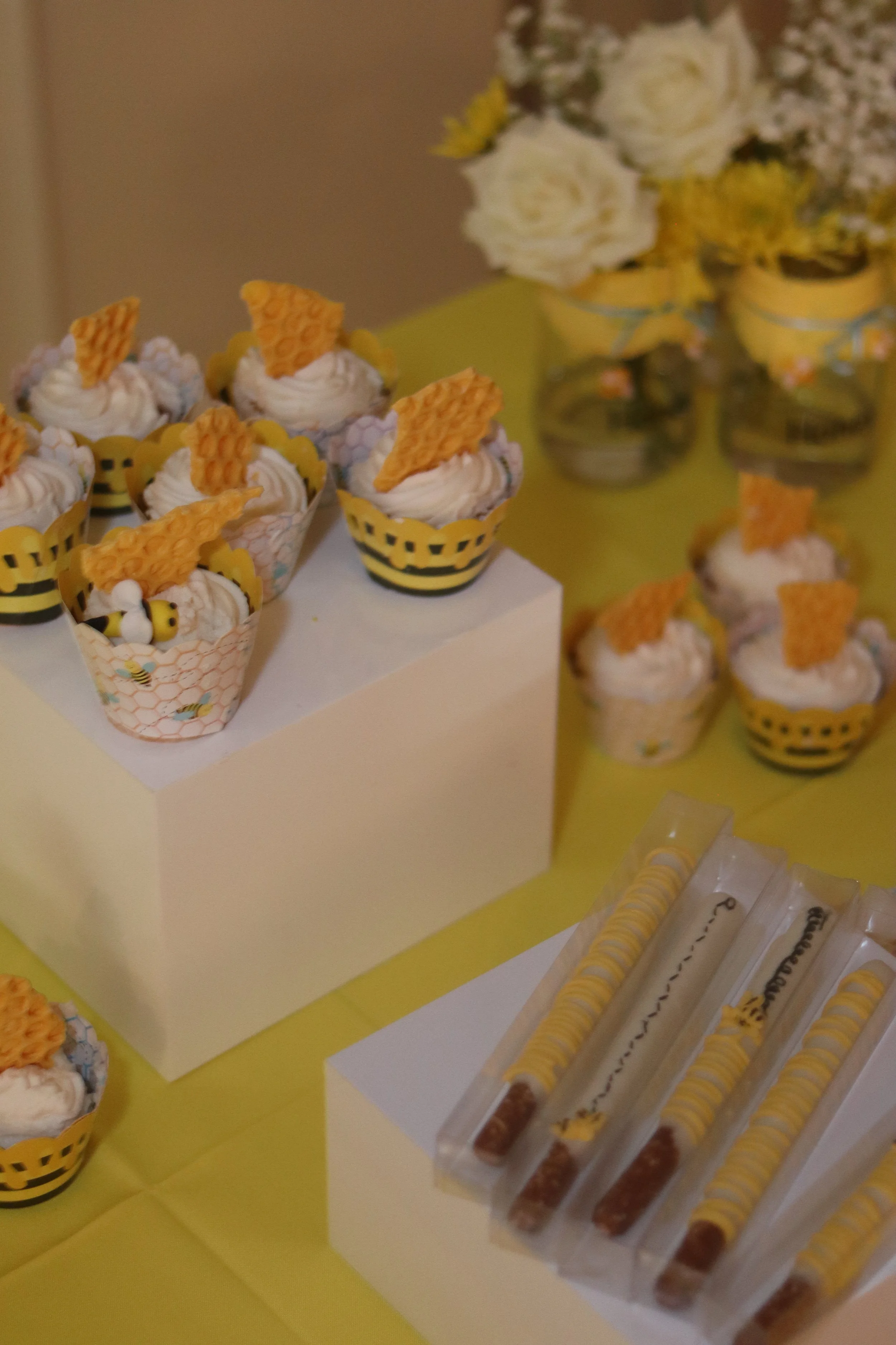 Party table with cupcakes decorated with bee and honeycomb theme, and honey sticks.