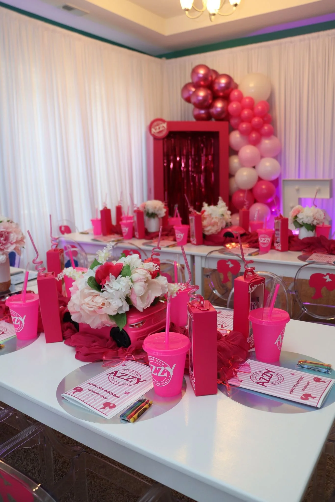 Decorated sweet sixteen birthday party table with pink and white balloons, floral centerpieces, pink cups and straws, and party favors on a white table, with a pink backdrop and 'Sweet 16' balloons in the background.