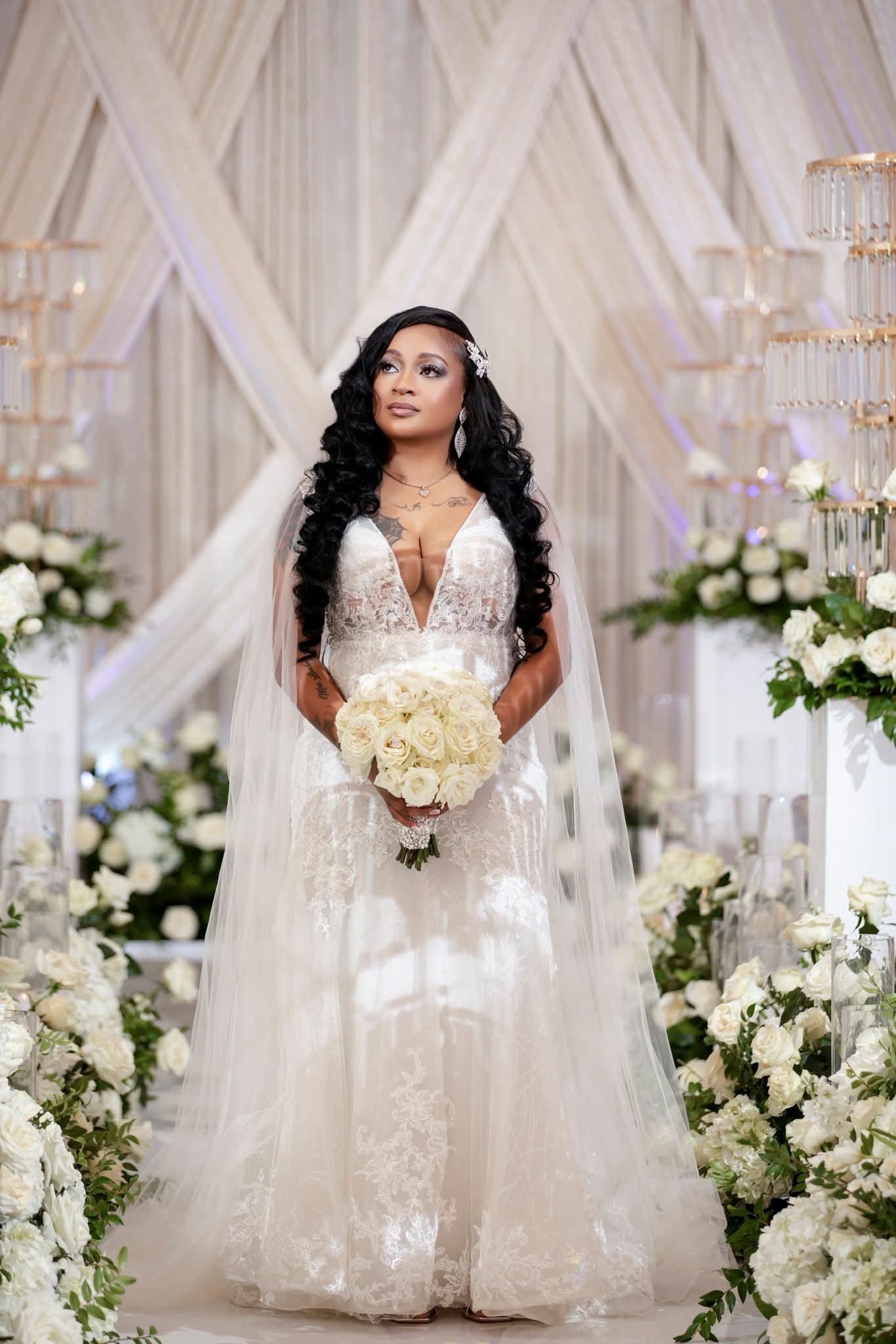 Woman in wedding dress holding bouquet surrounded by white flowers and candles in an elegant indoor wedding venue.