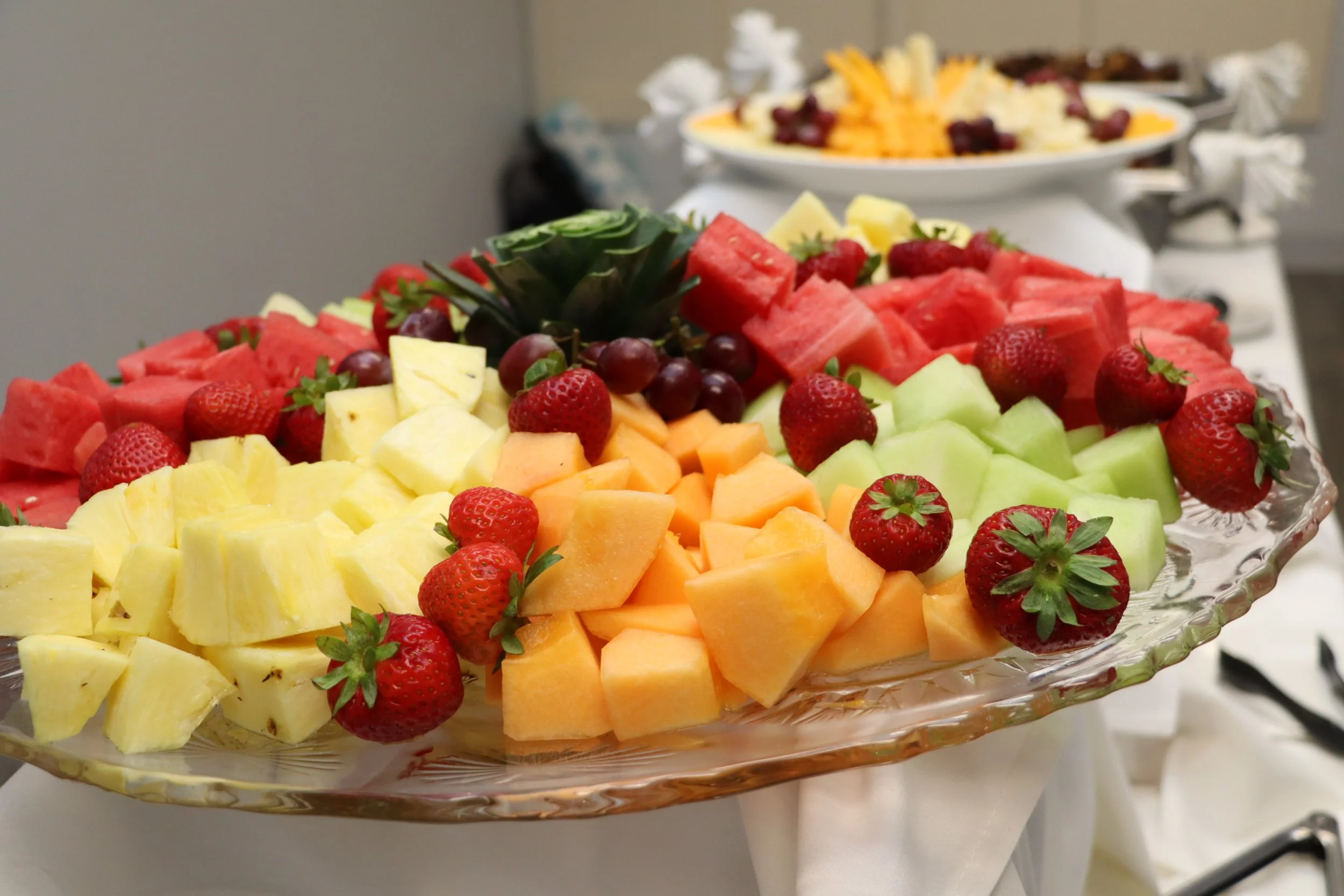 Assorted sliced fruit including pineapple, watermelon, cantaloupe, honeydew, strawberries, and grapes on a glass platter.