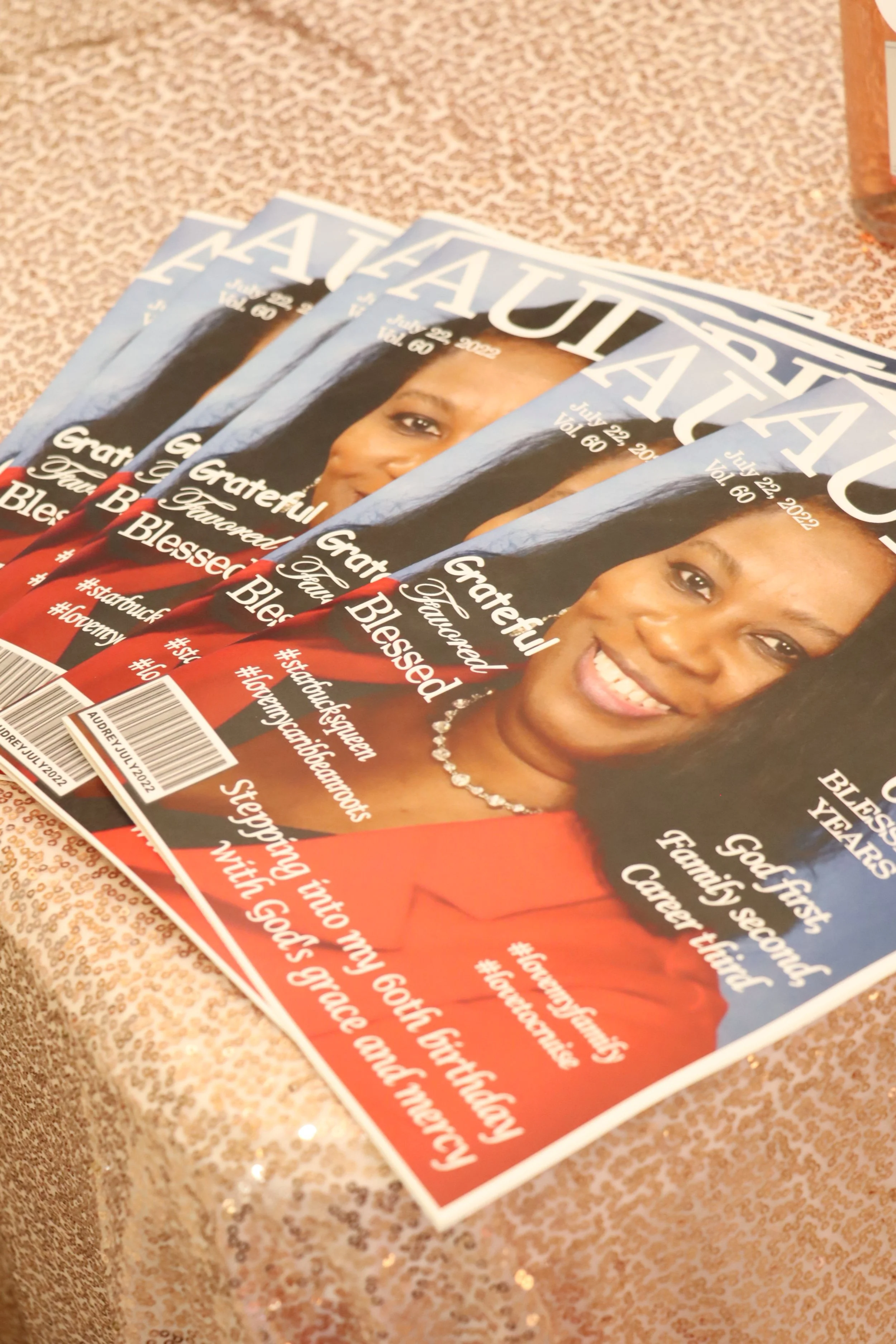 Magazines titled 'AUDREY' with a smiling woman on the cover, placed on a glittery surface.