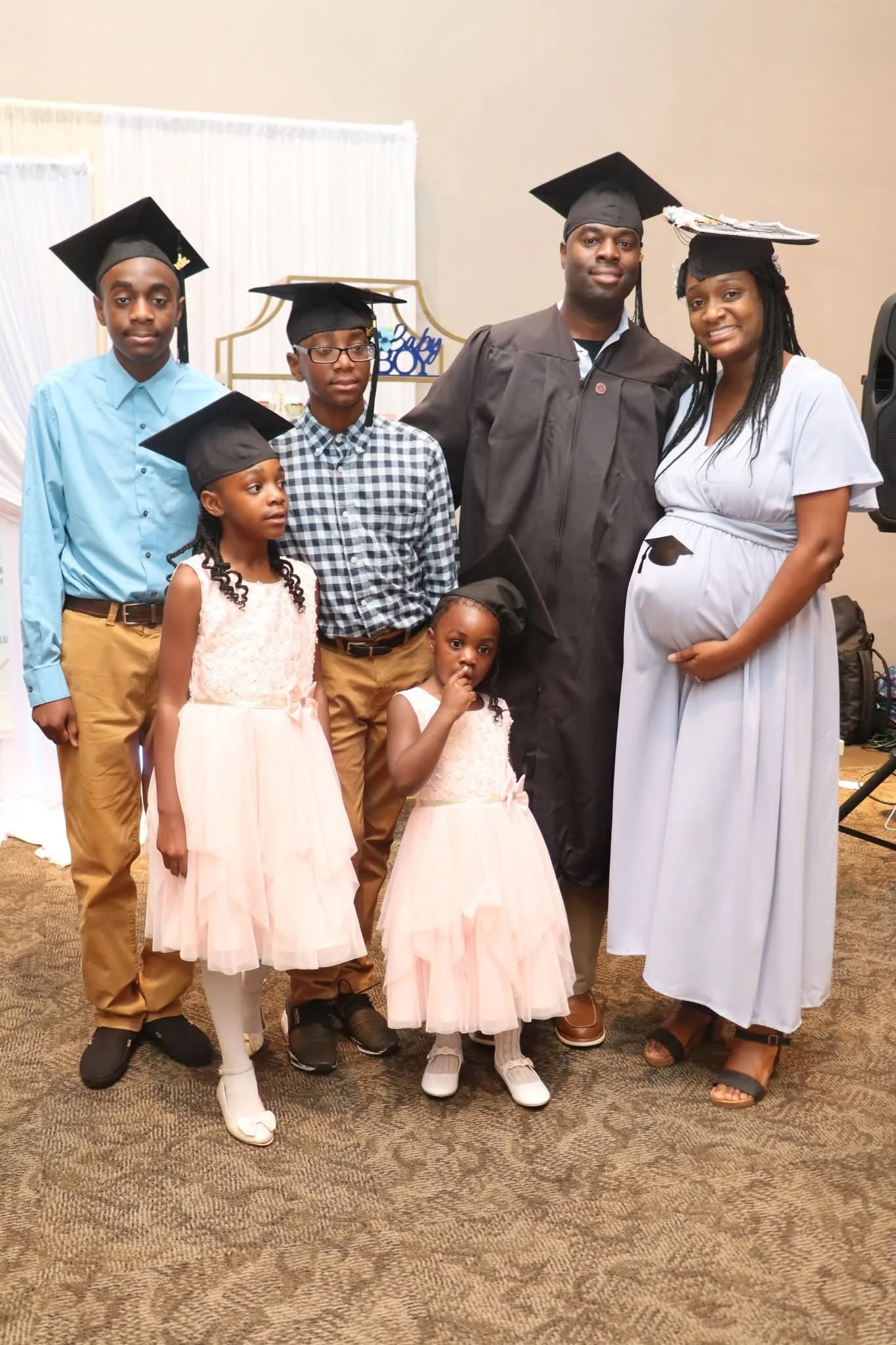 A family celebrating a graduation, with graduates wearing caps and gowns, posing together indoors.