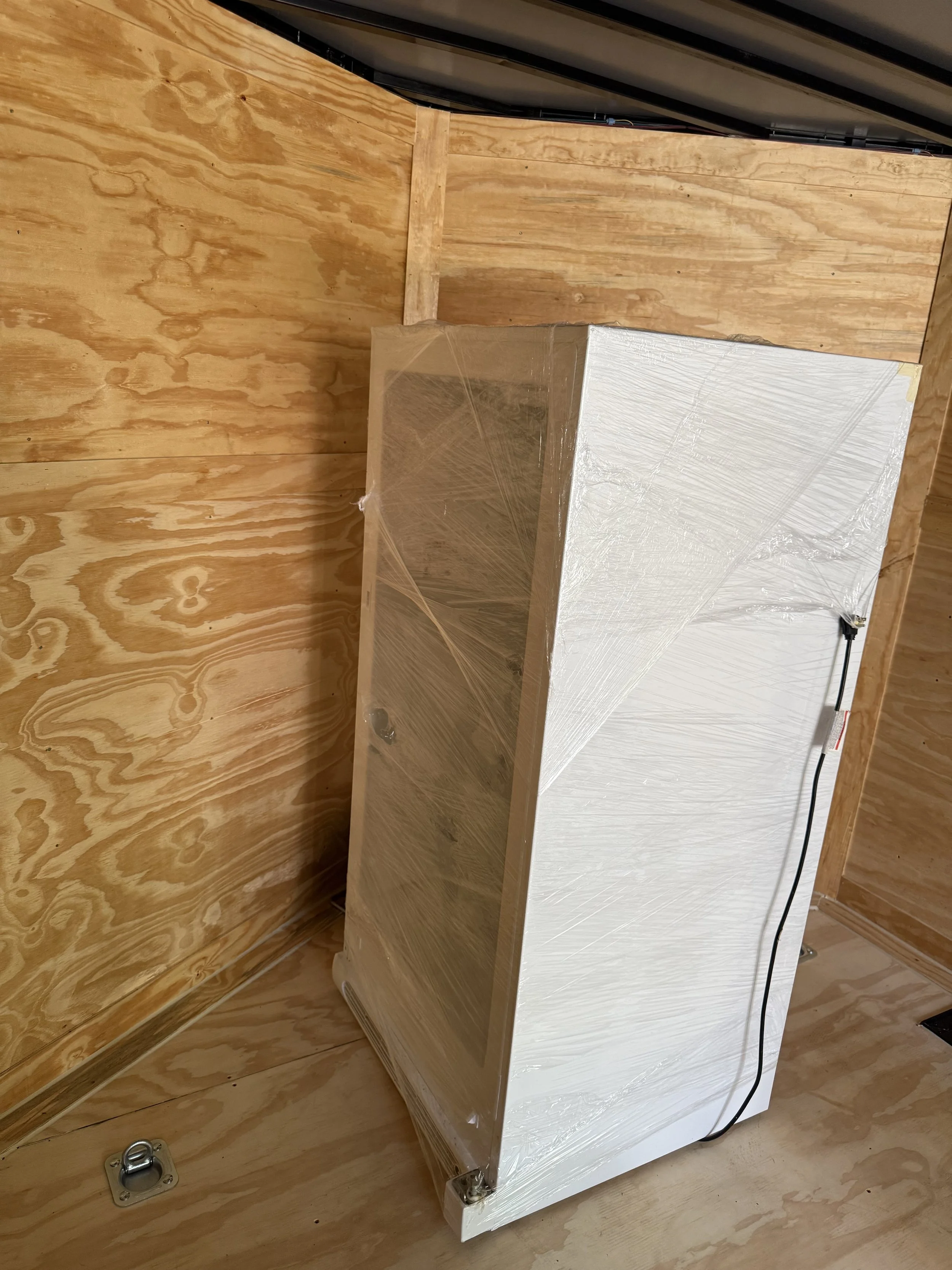 White appliance wrapped in plastic, installed in a wooden room, with a power cord attached.