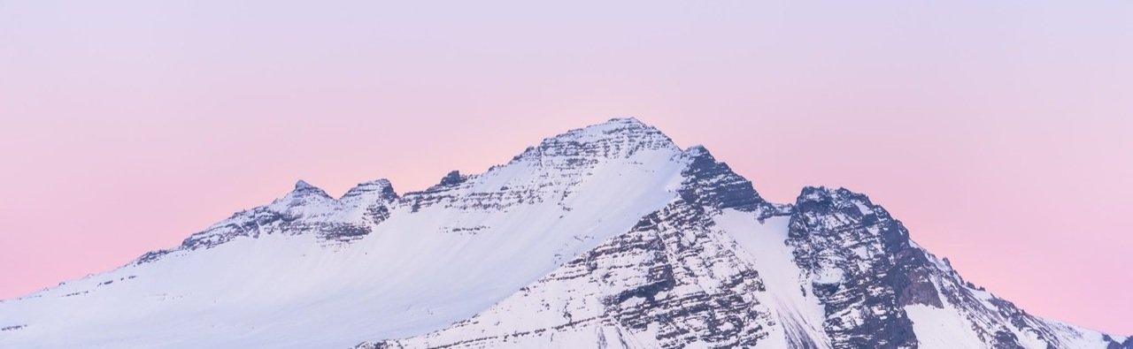 Snow‑capped mountain peaks under a pink sky at sunrise or sunset, symbolising a new horizon and the scale of global M&A
