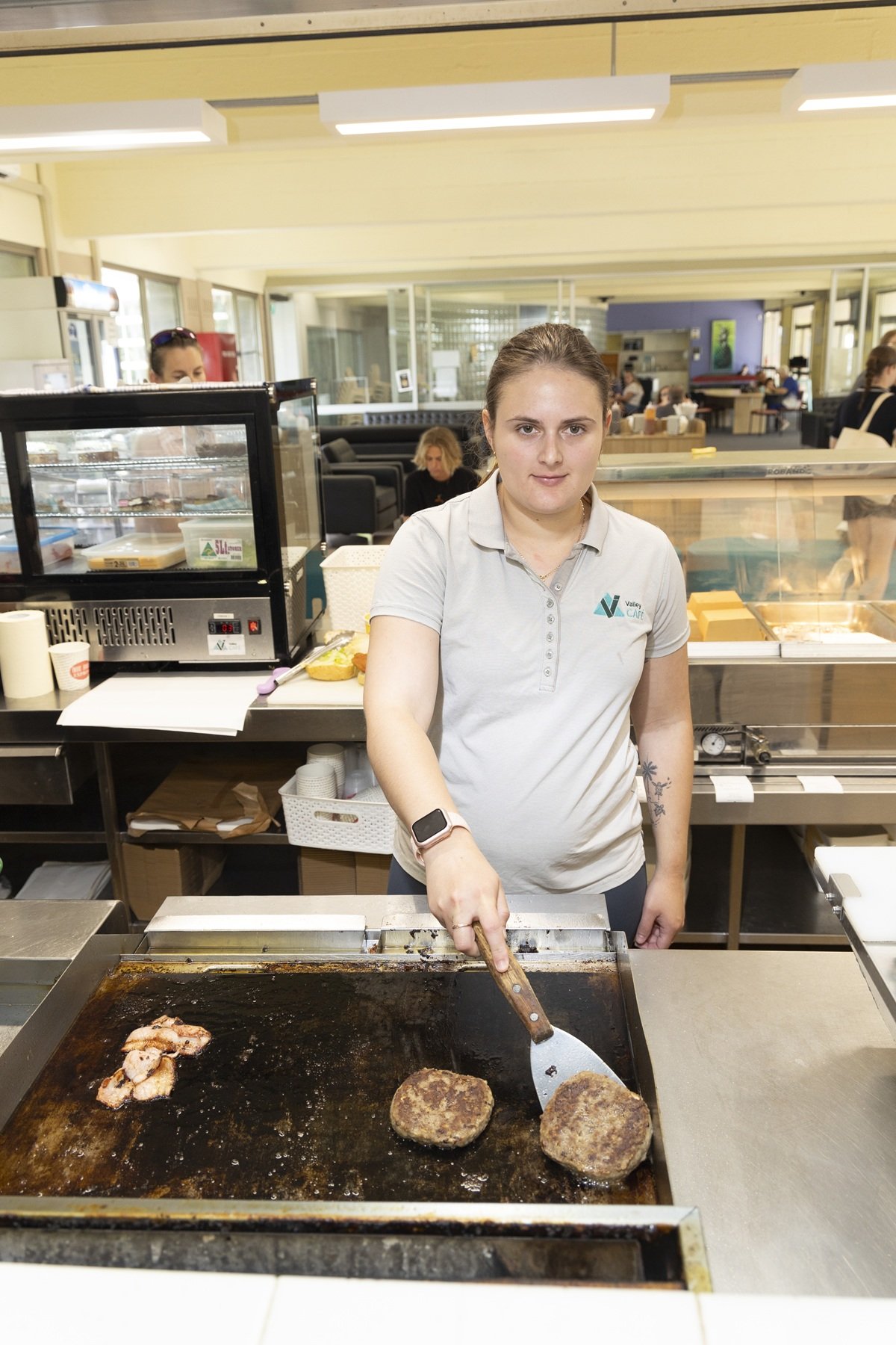 A woman cooking hamburger patties on a flat-top grill in our Valley TAFE Canteen.