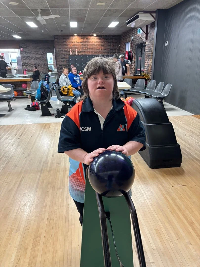 A young Valley client wearing a bowling shirt holding a bowling ball at a bowling alley.