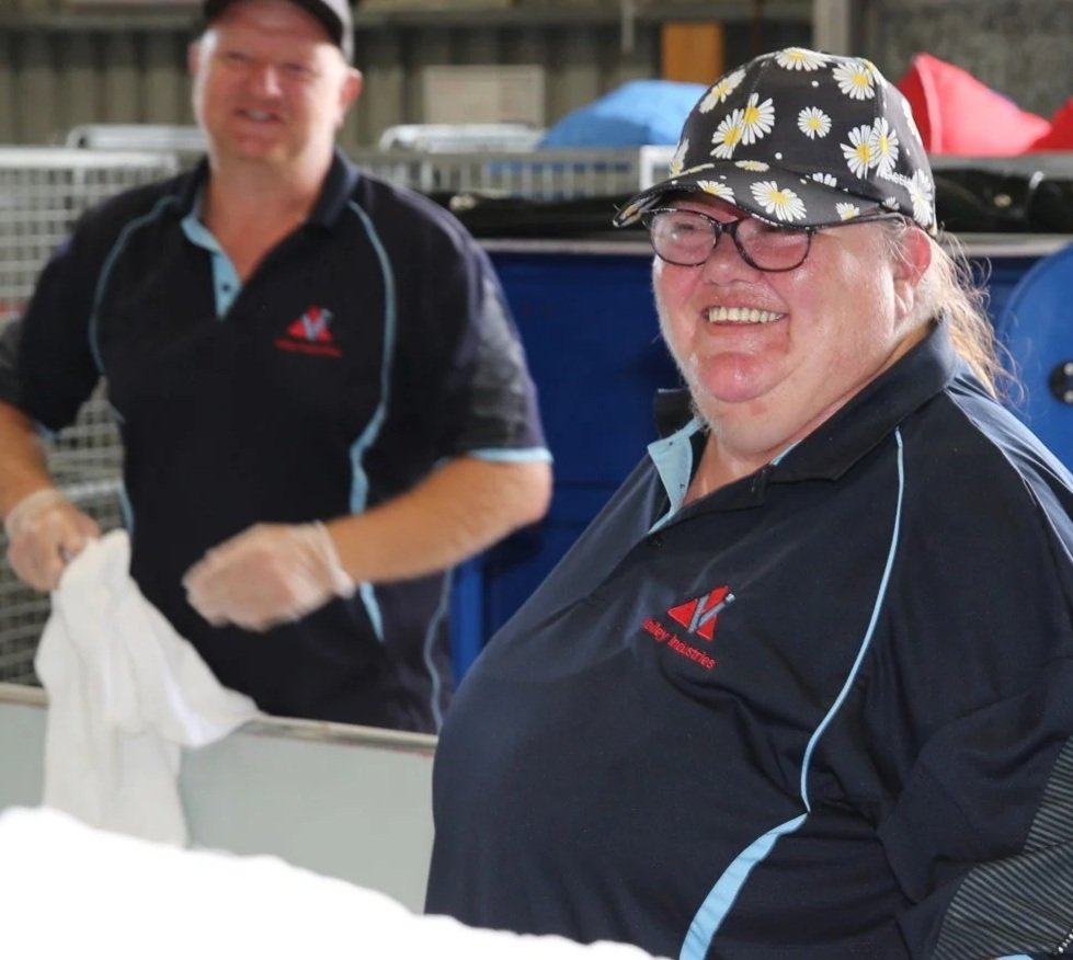 Two smiling men in black and light blue uniforms working at a laundry and linen facility.