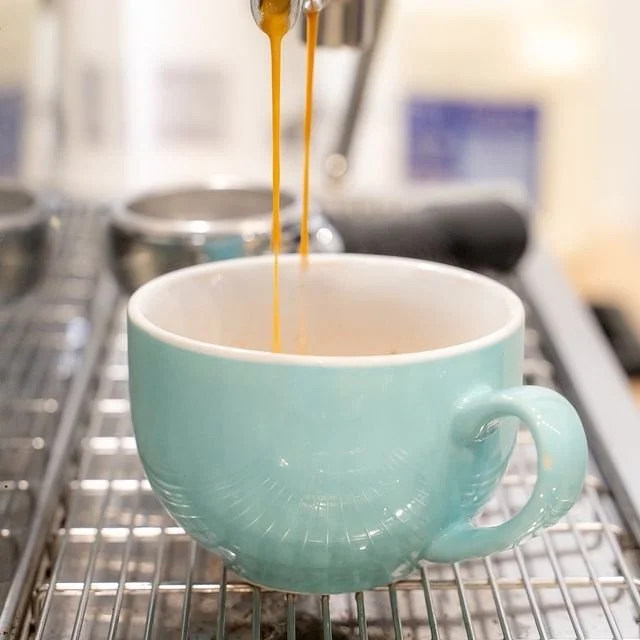 Stream of espresso being poured into a light blue coffee cup on a metal grate in our Valley TAFE Canteen.