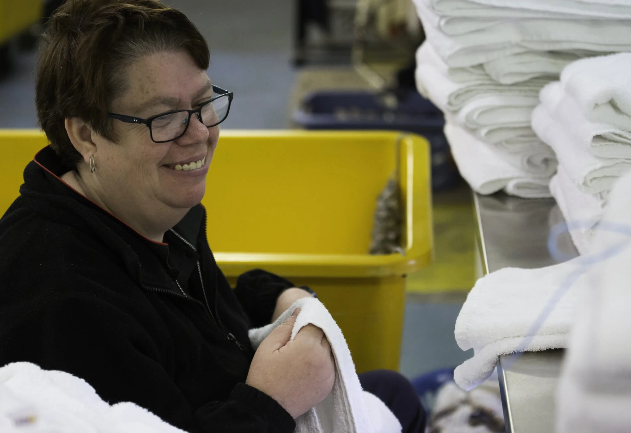 A woman smiling at her work with white towels or cloths on a table in an industrial setting.