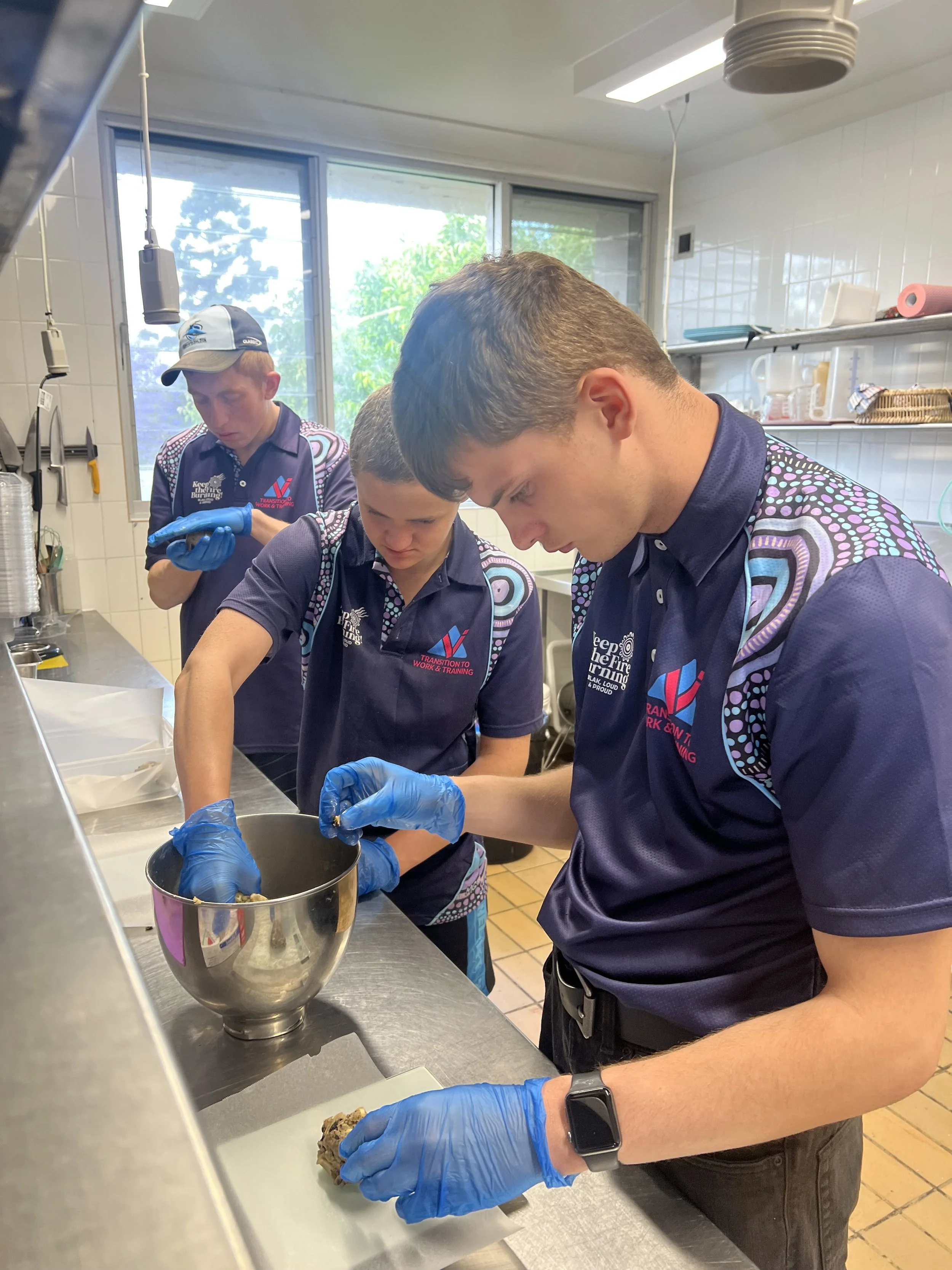 Four Valley team members preparing cookie dough or similar treats in a commercial kitchen, with cookies on a tray in the foreground.