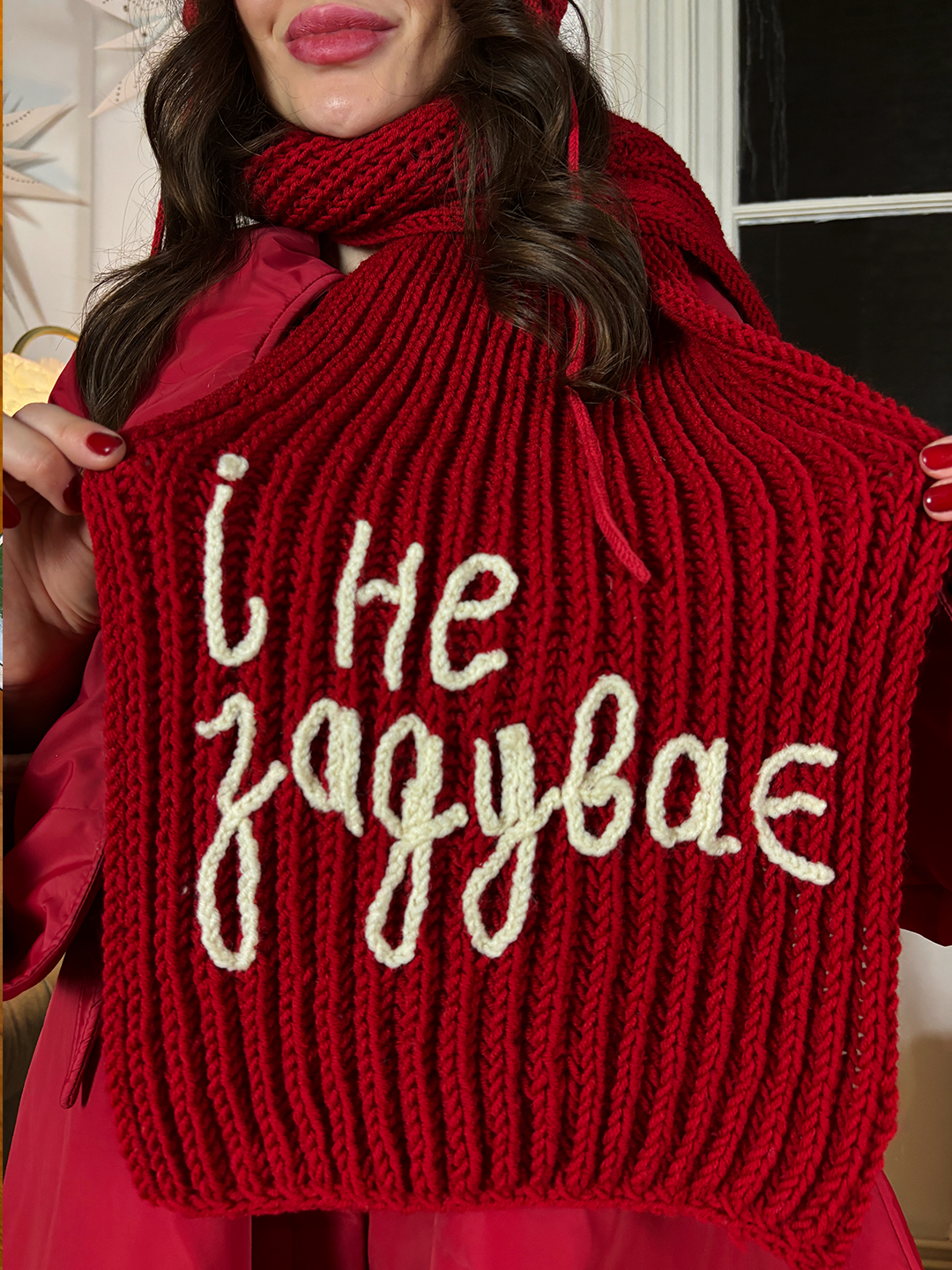 Red knitted scarf with the text “і не задуває.” 100% of the profit supports Ukrainian pensioners