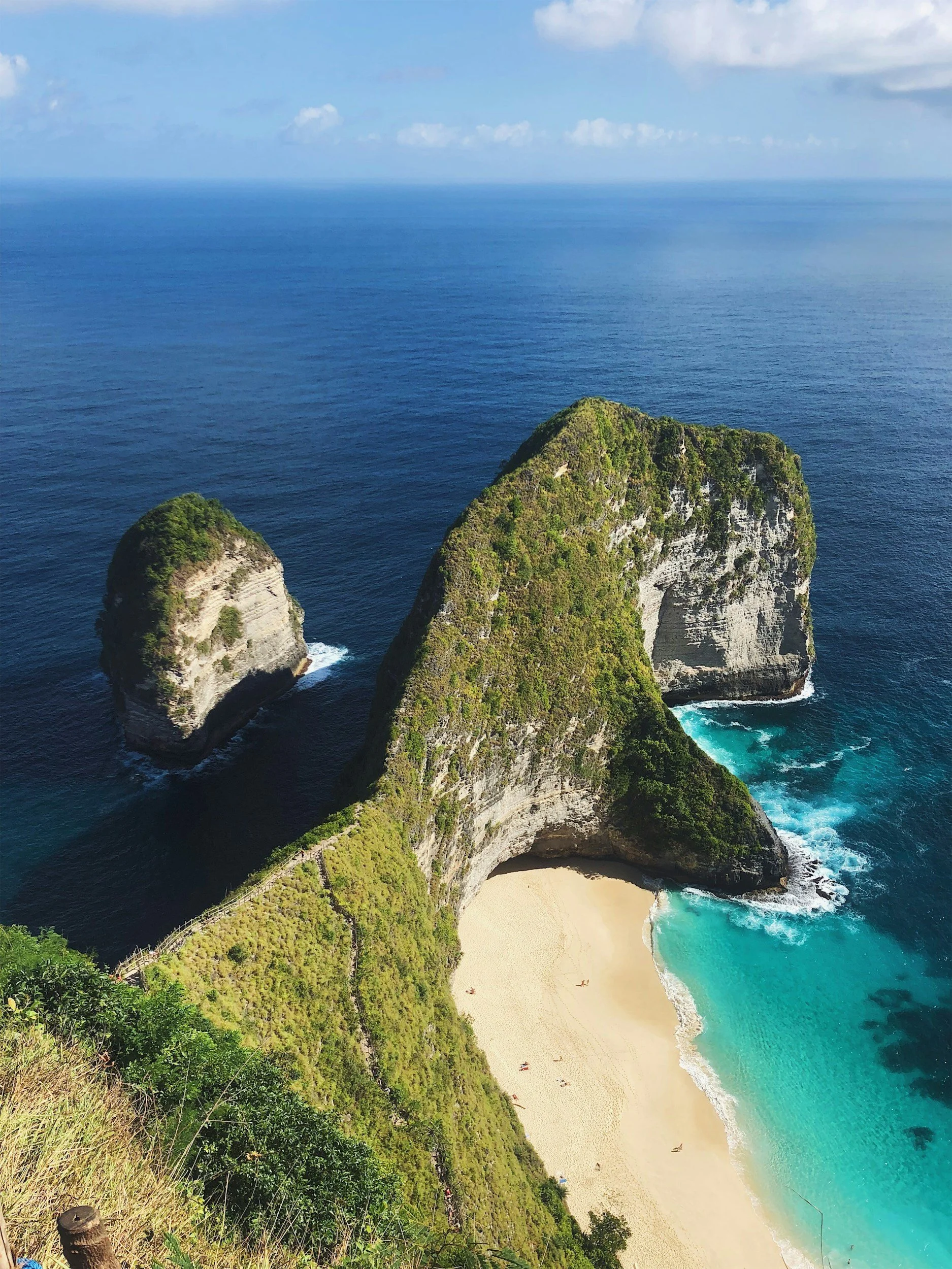 Aerial view of Nusa Penida, a small island off Bali, featuring sandy beach, lush green cliffs, and blue ocean water.